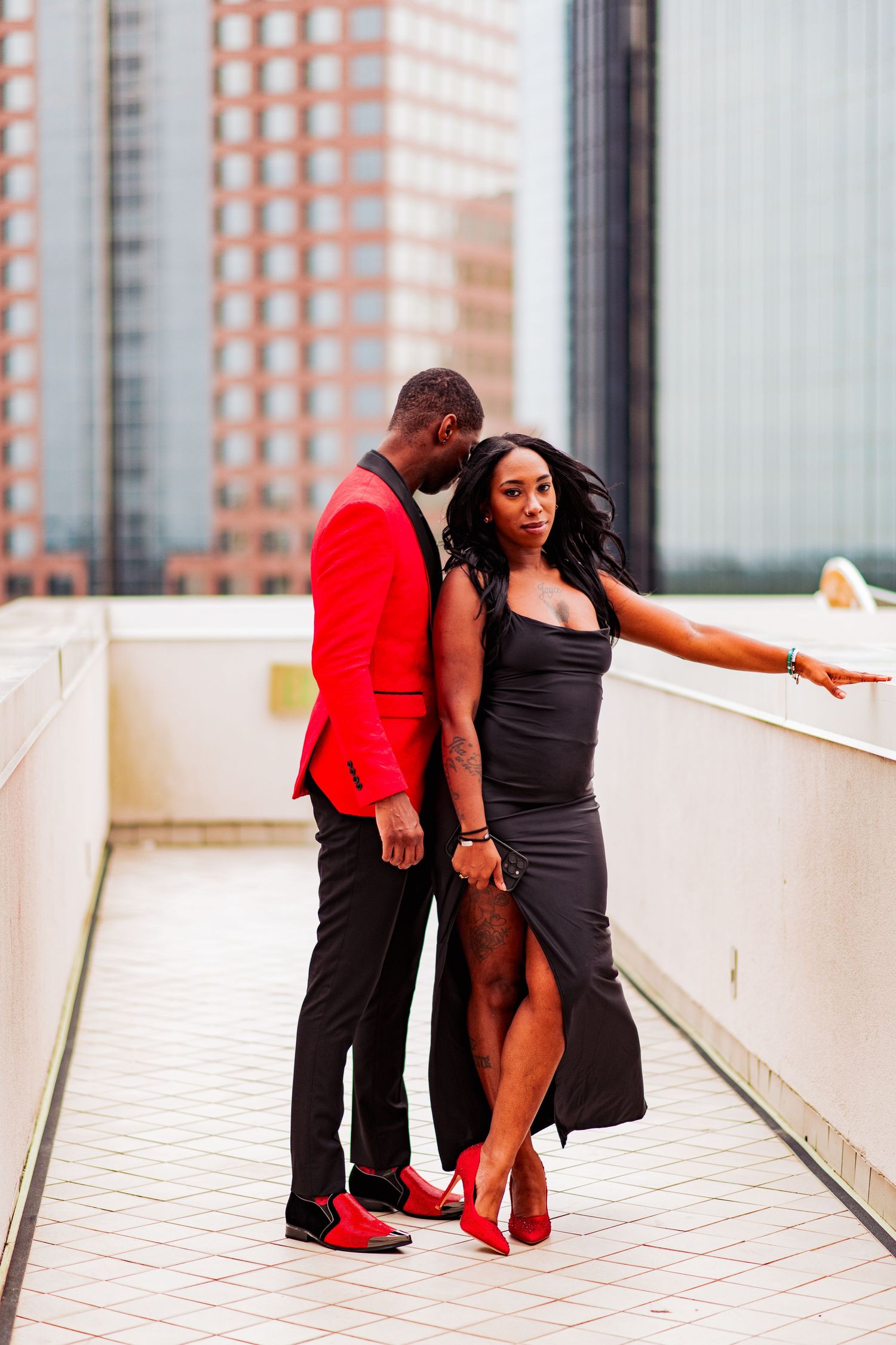Artistic portrait series showing couple in black and red outfits posing against modern urban architecture.