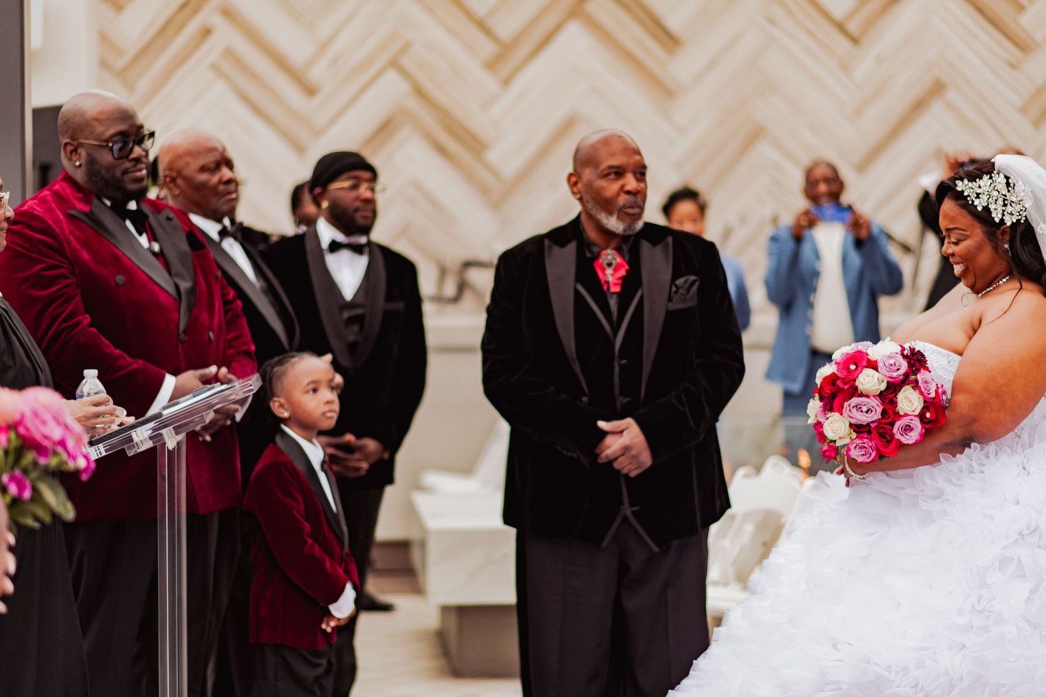 Wedding ceremony in an elegant venue with chevron pattern walls and formal attire.