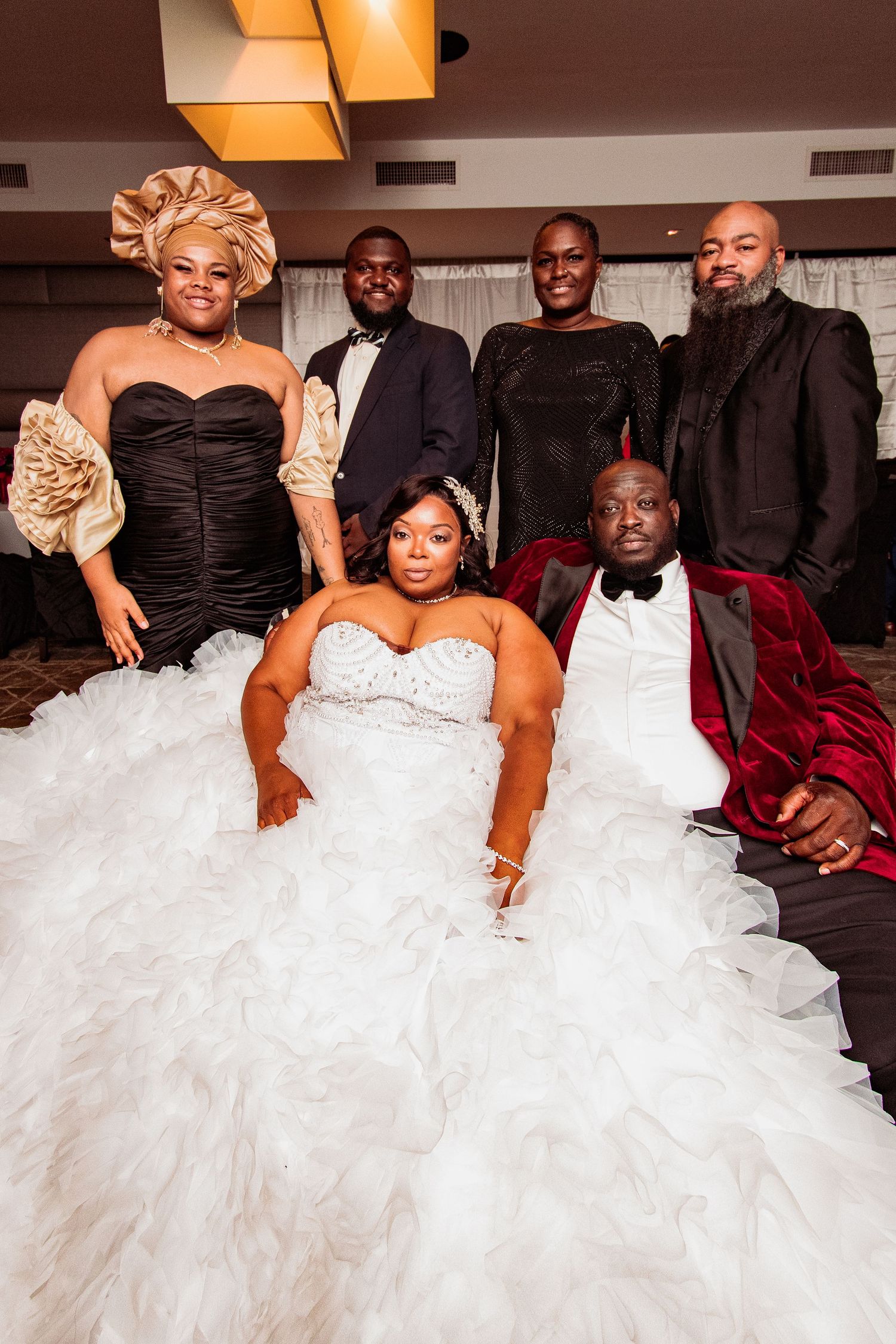 A wedding party poses together in formal attire with the bride wearing a dramatic white ruffled gown.