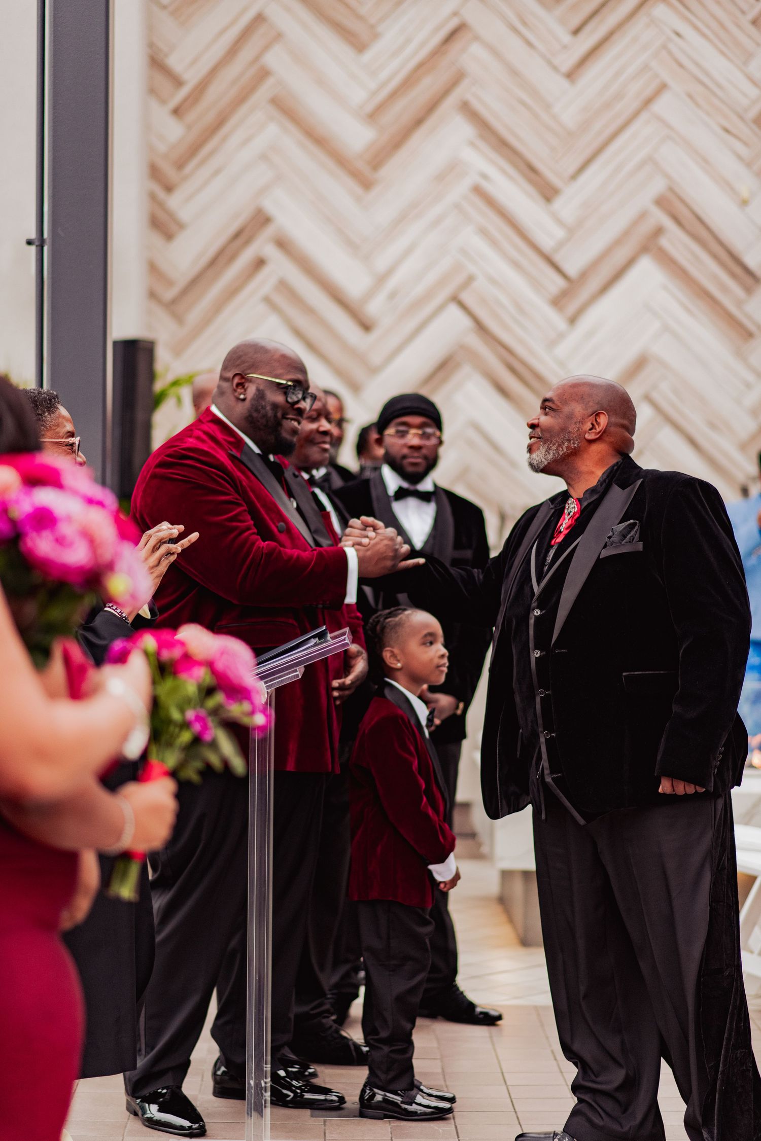 Wedding party members in burgundy and black suits dancing and celebrating in an elegant venue.