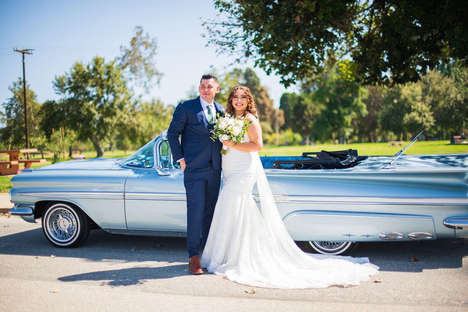 Bride in white gown and groom in navy suit pose with classic silver automobile Legg Lake Park, Whittier Narrows Recreation Area.