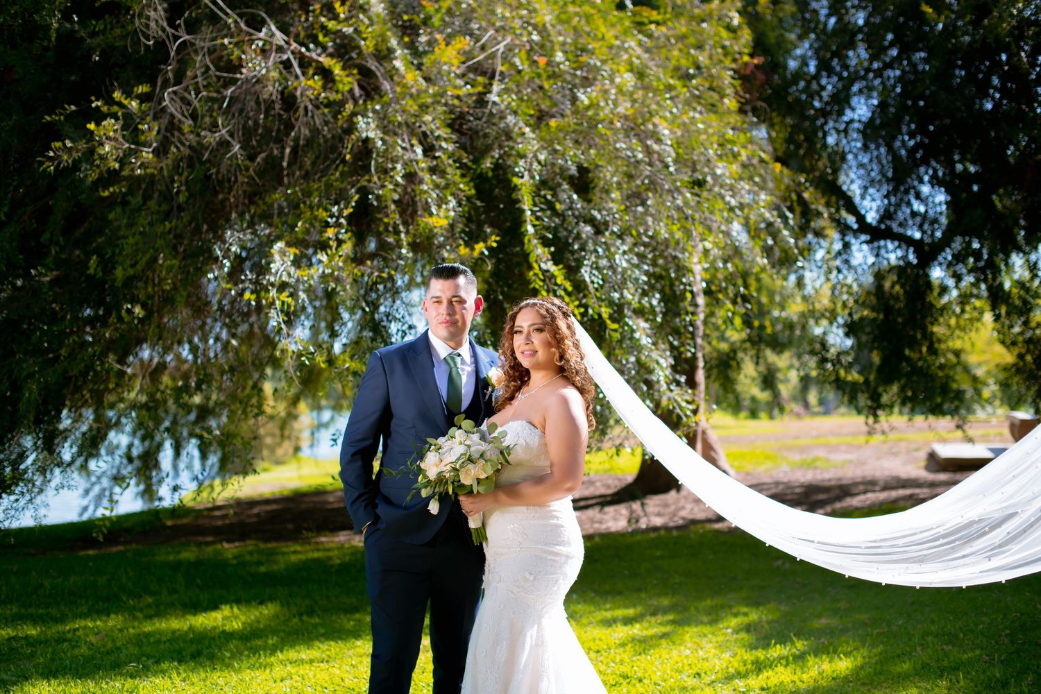Wedding portraits in a sunlit garden setting with flowing white veil and natural scenery.