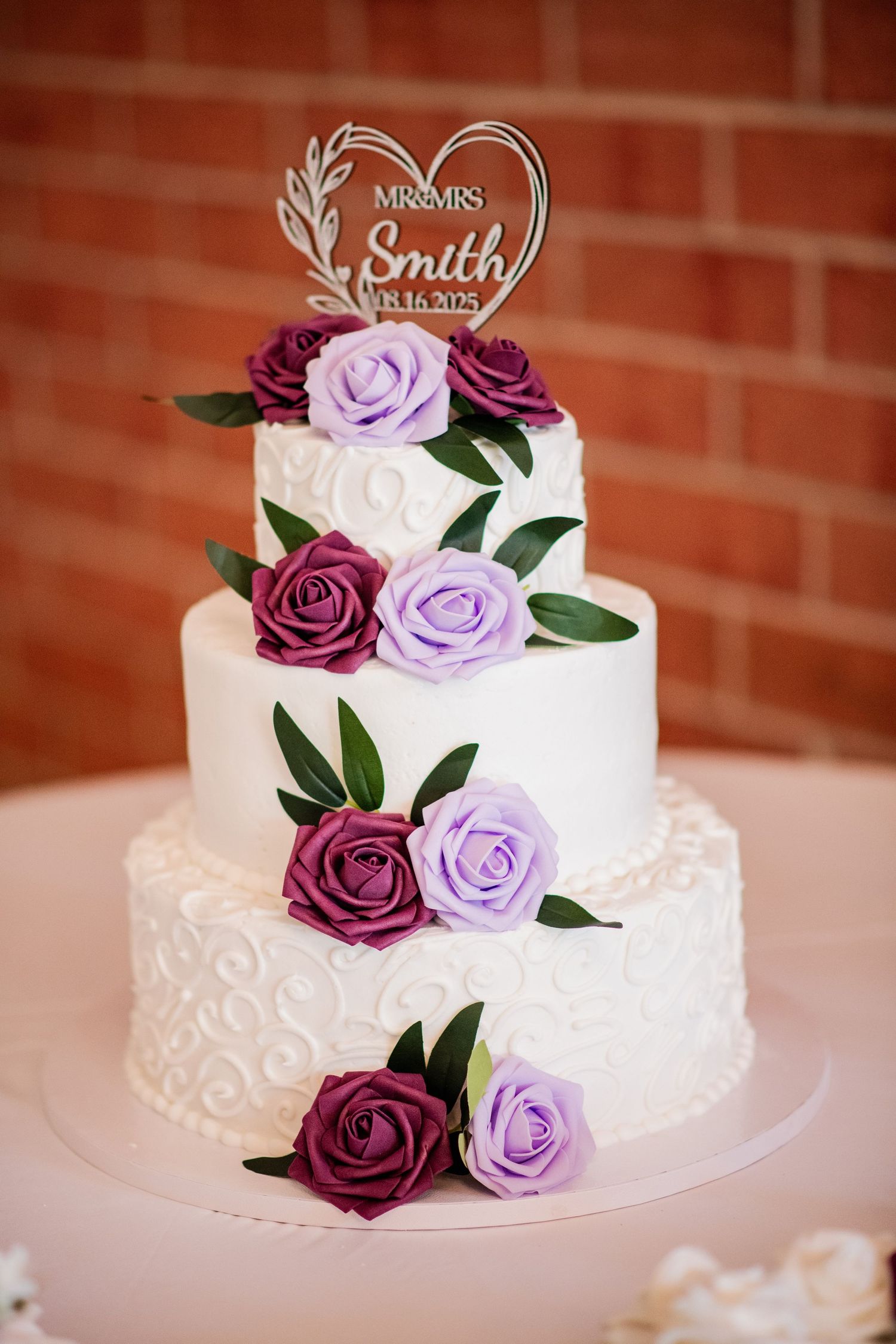 White tiered wedding cake decorated with purple and lavender roses and Mr & Mrs cake topper.