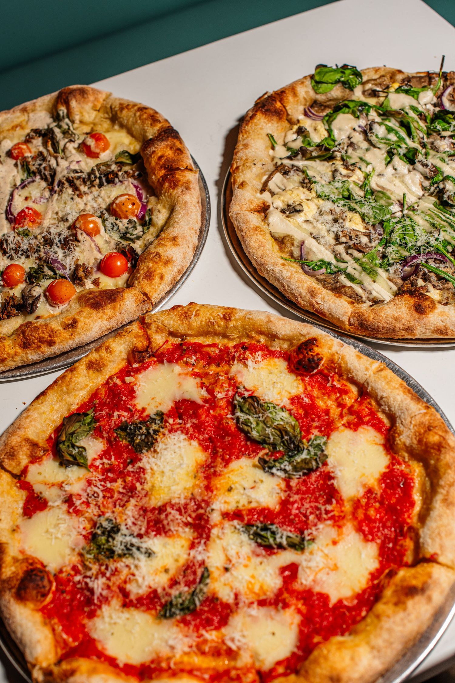Close-up view of Neapolitan pizzas with red sauce, melted mozzarella, and fresh basil on metal serving plates.