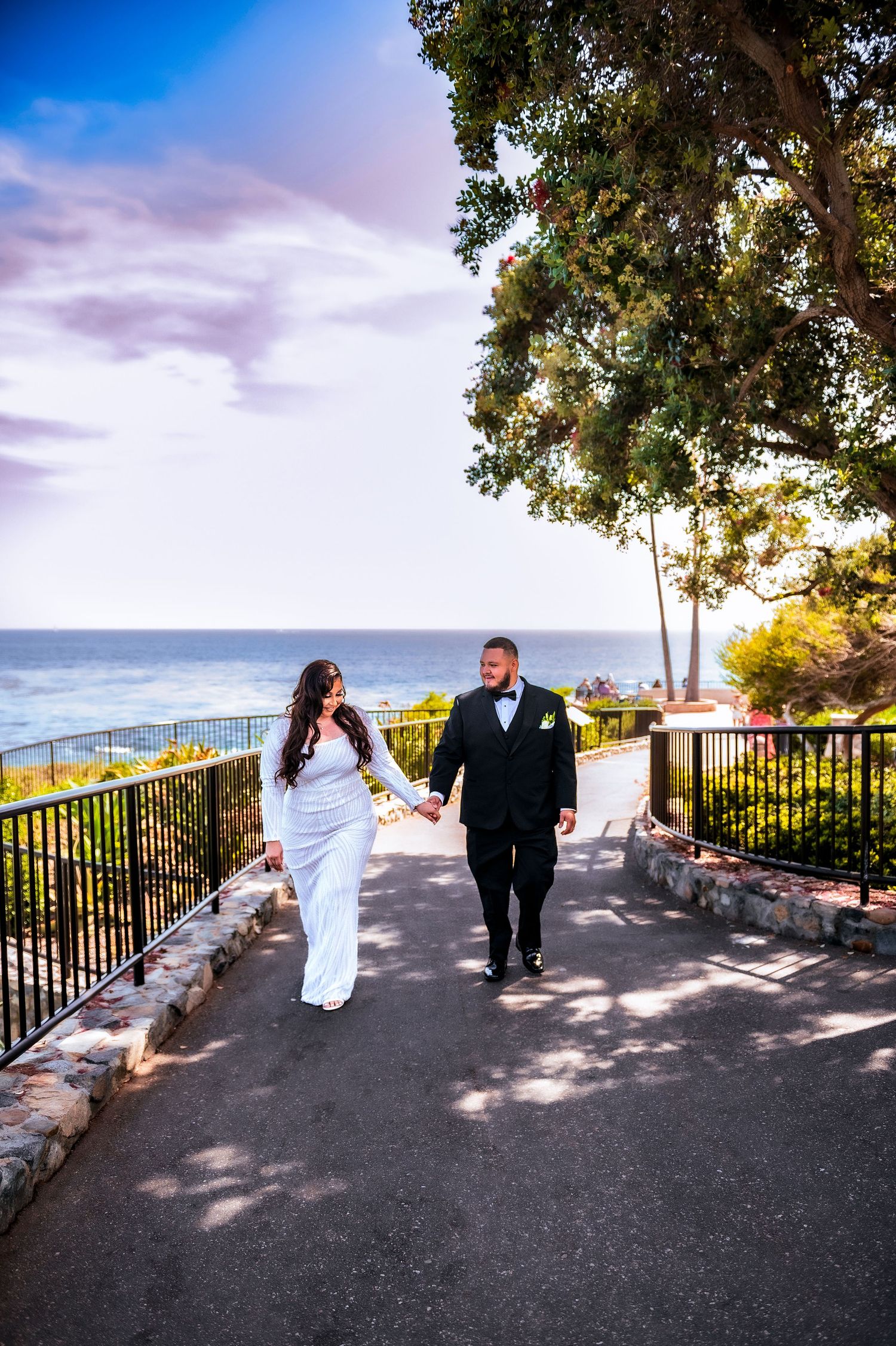 A couple poses playfully in a sequence of photos on a scenic overlook with ocean views and iron railings.