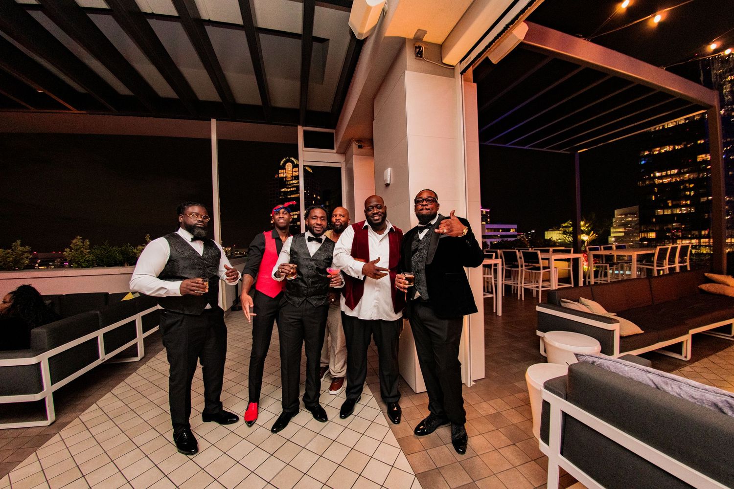 Group celebrating at a stylish rooftop venue with city lights in the background.
