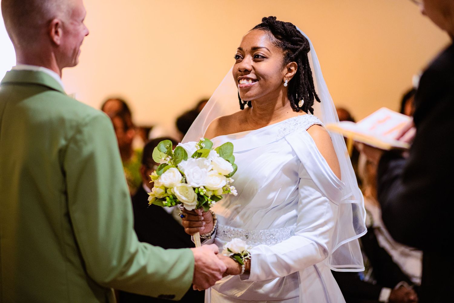 A joyful moment during a wedding ceremony as the bride in white holds a bouquet of white flowers.