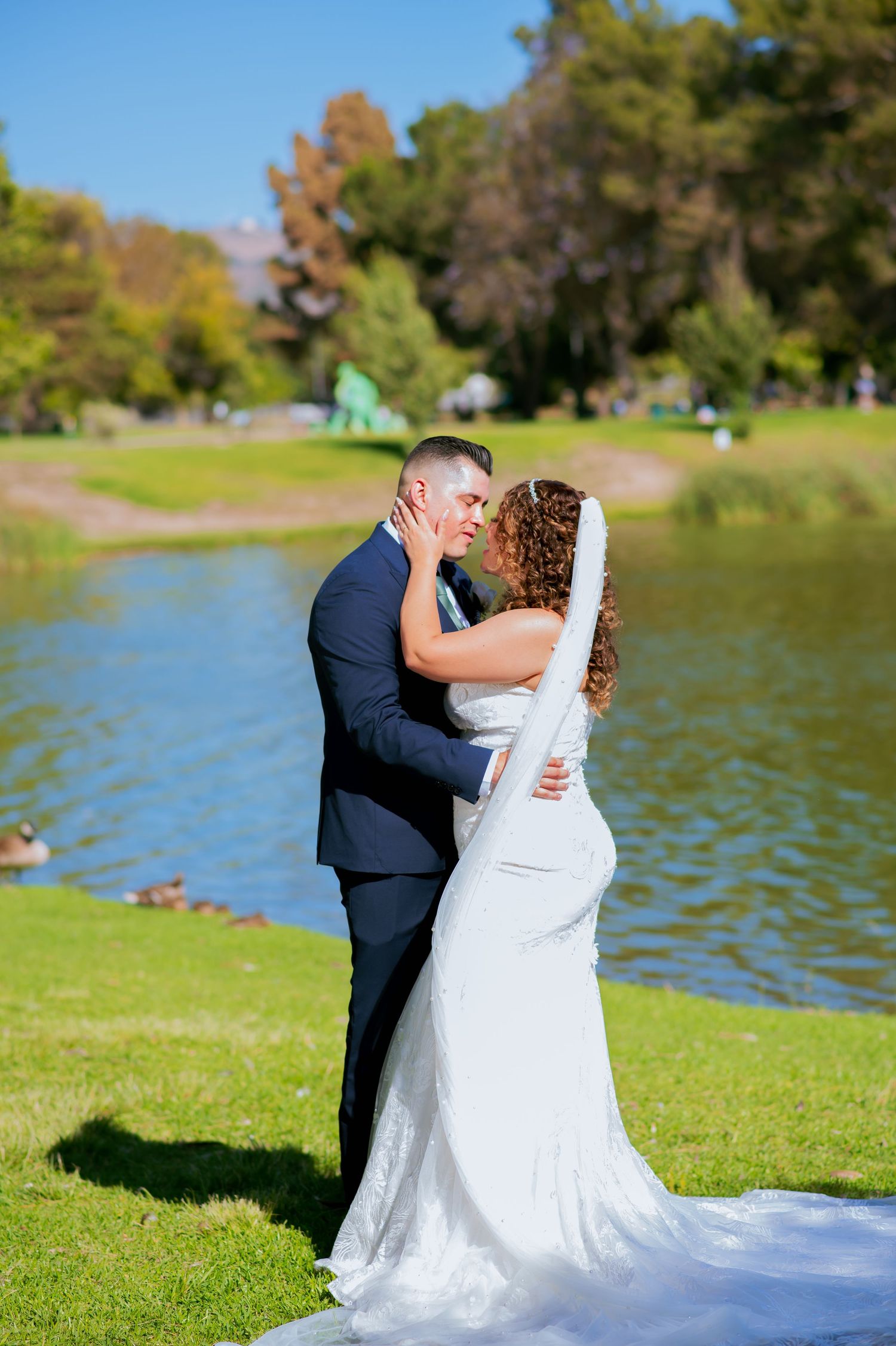 Wedding couple shares romantic kiss on scenic lakefront with flowing white gown in South El Monte.