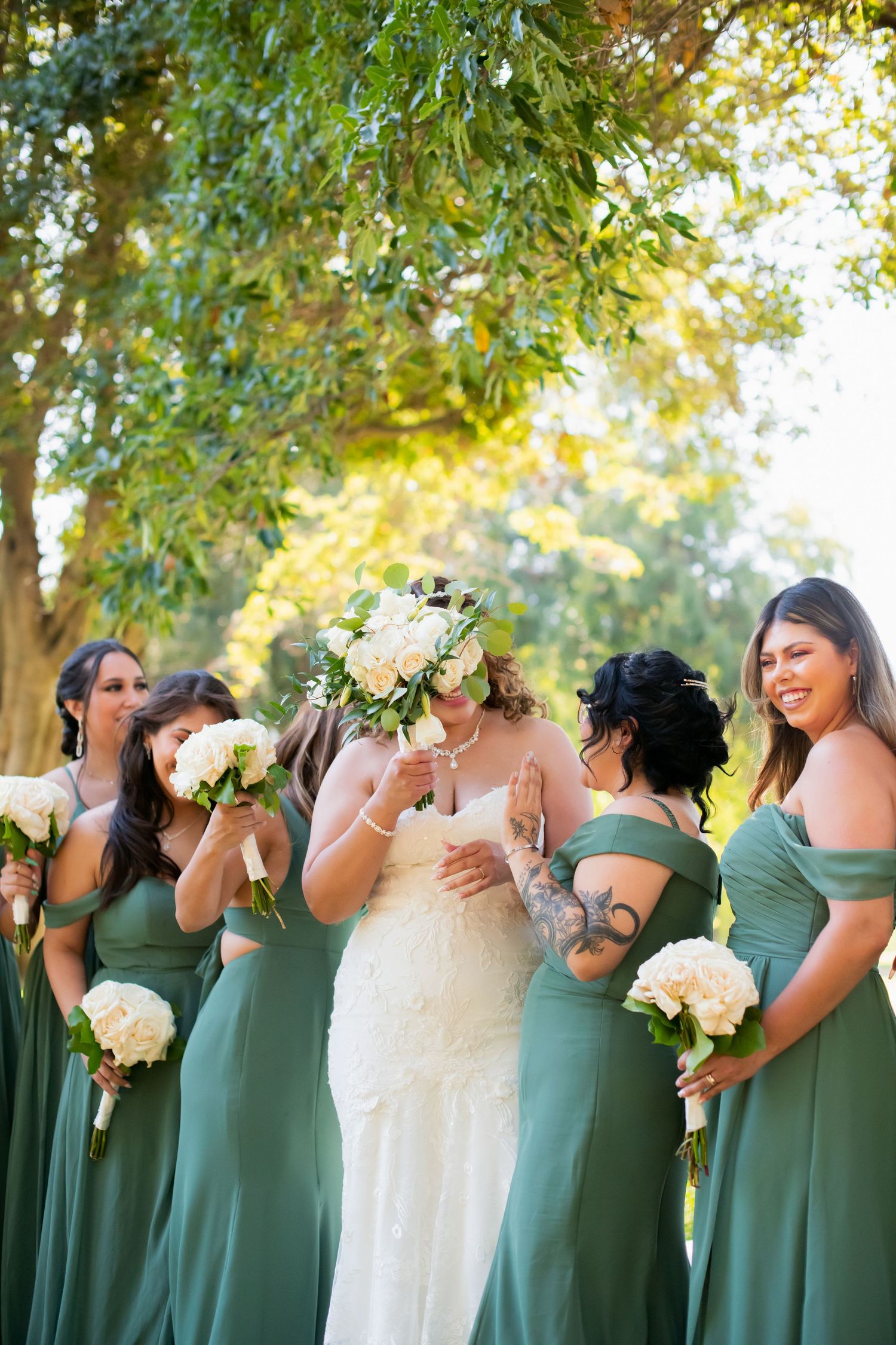 Bridal party in sage green dresses poses informally during outdoor wedding photography session.