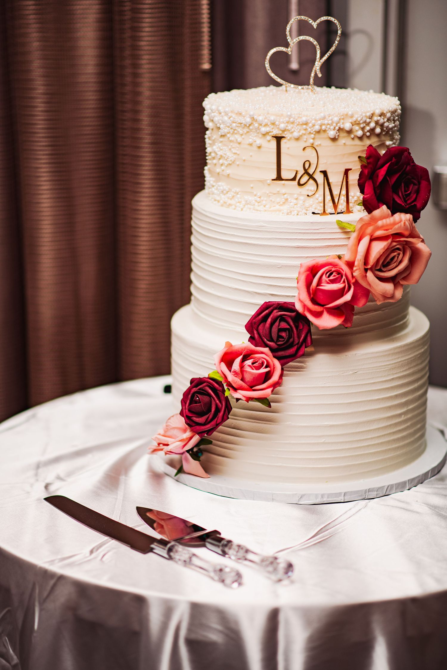 Elegant white wedding cake decorated with burgundy and pink roses on a white tablecloth.