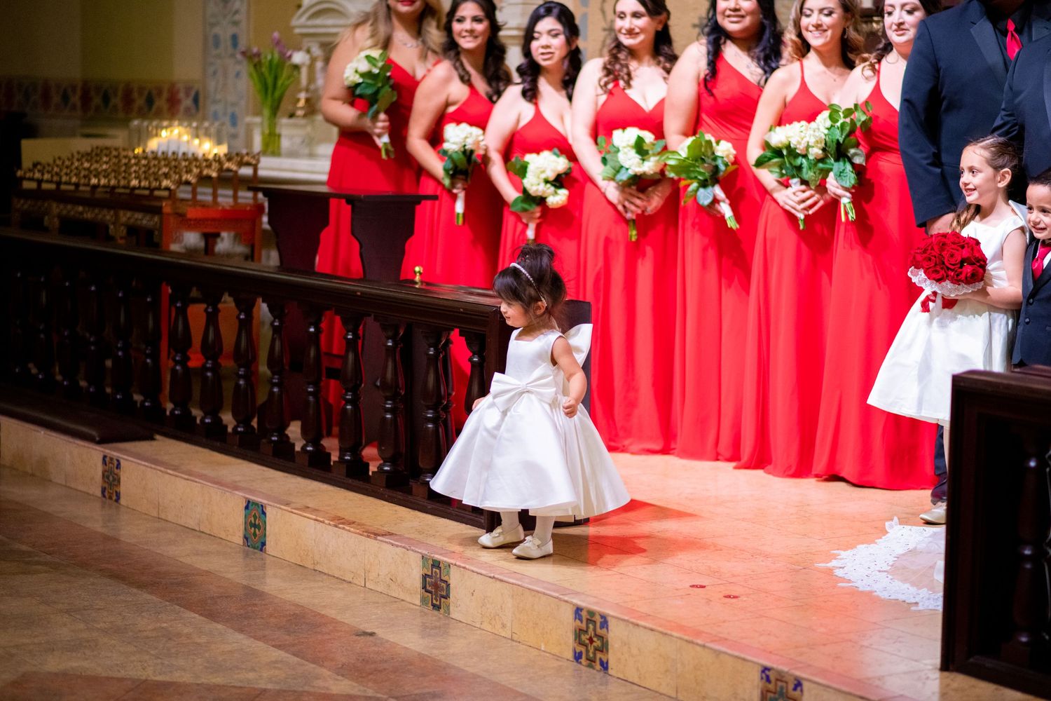 A wedding party in red dresses and formal attire poses together in a church sanctuary.