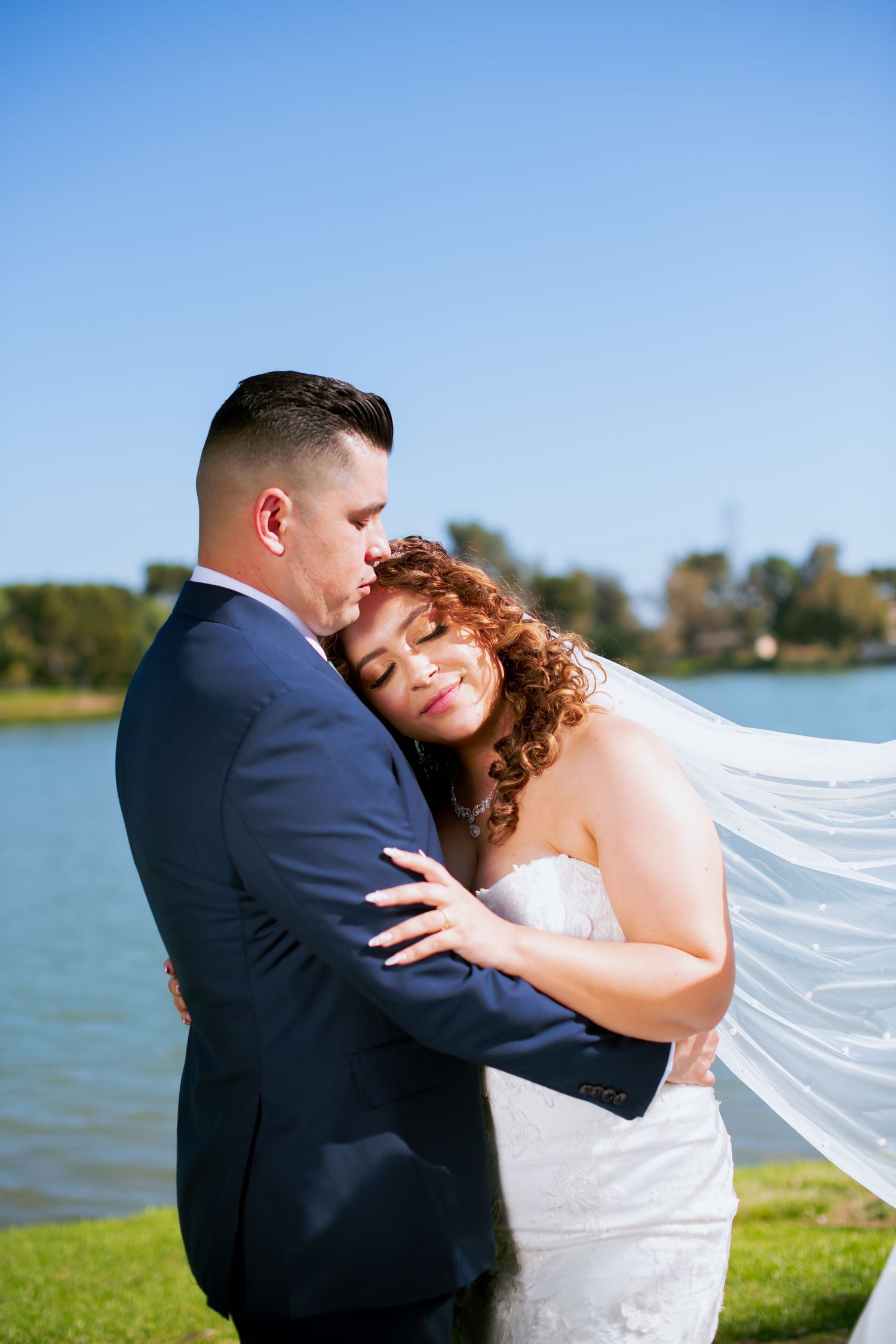 Romantic wedding portrait showing tender moment between couple by lakeside.