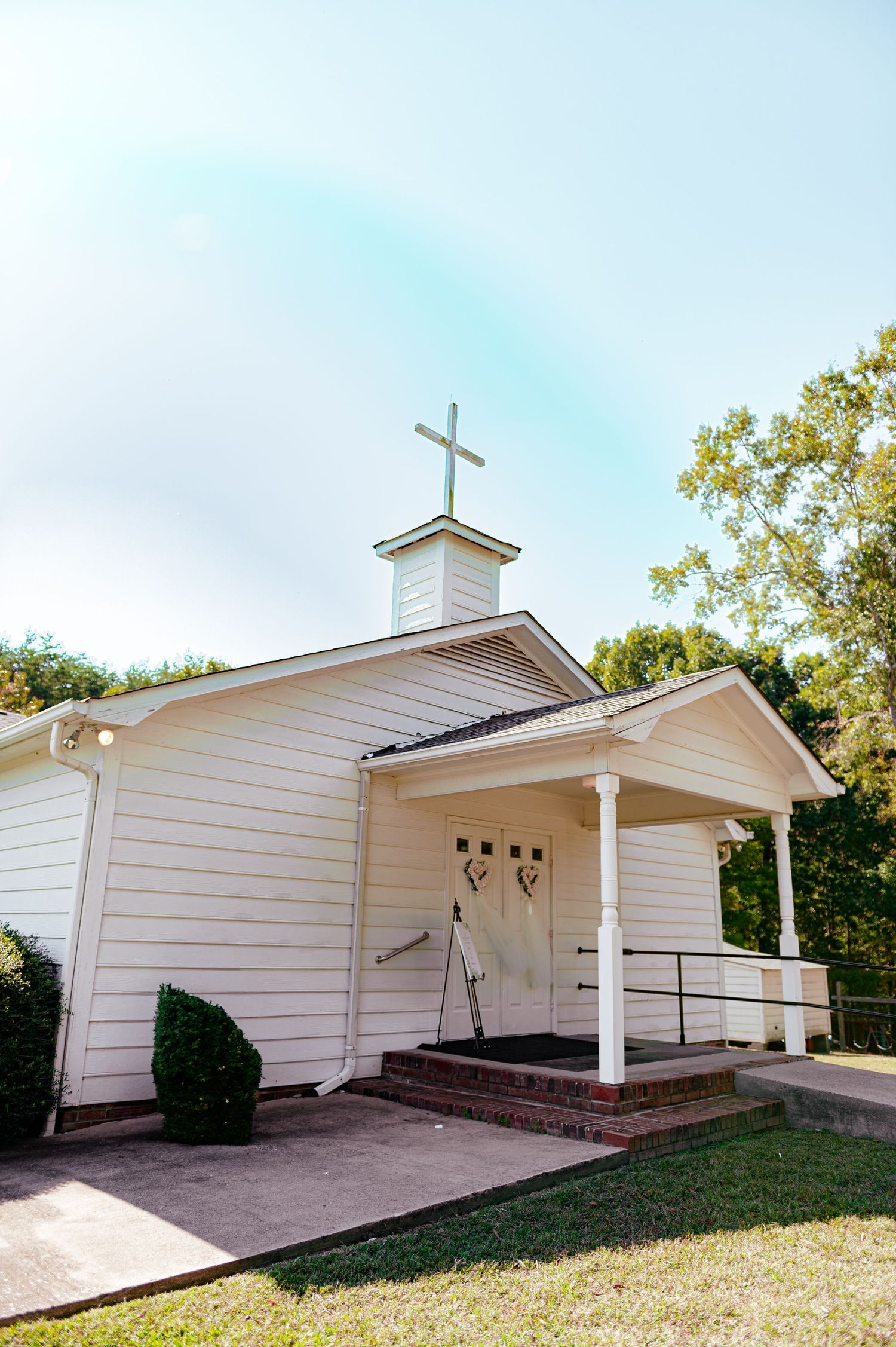 Small white country church with a cross on top and wheelchair ramp access under a bright sky.