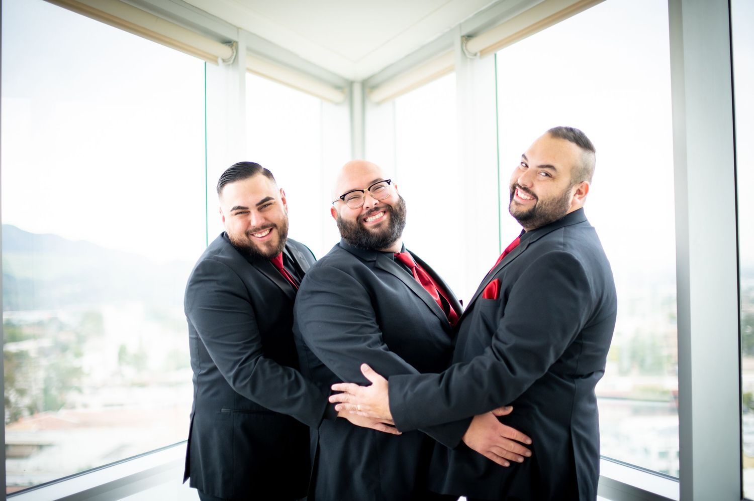 Three people in black suits share joyful laughter together in a bright modern office setting.