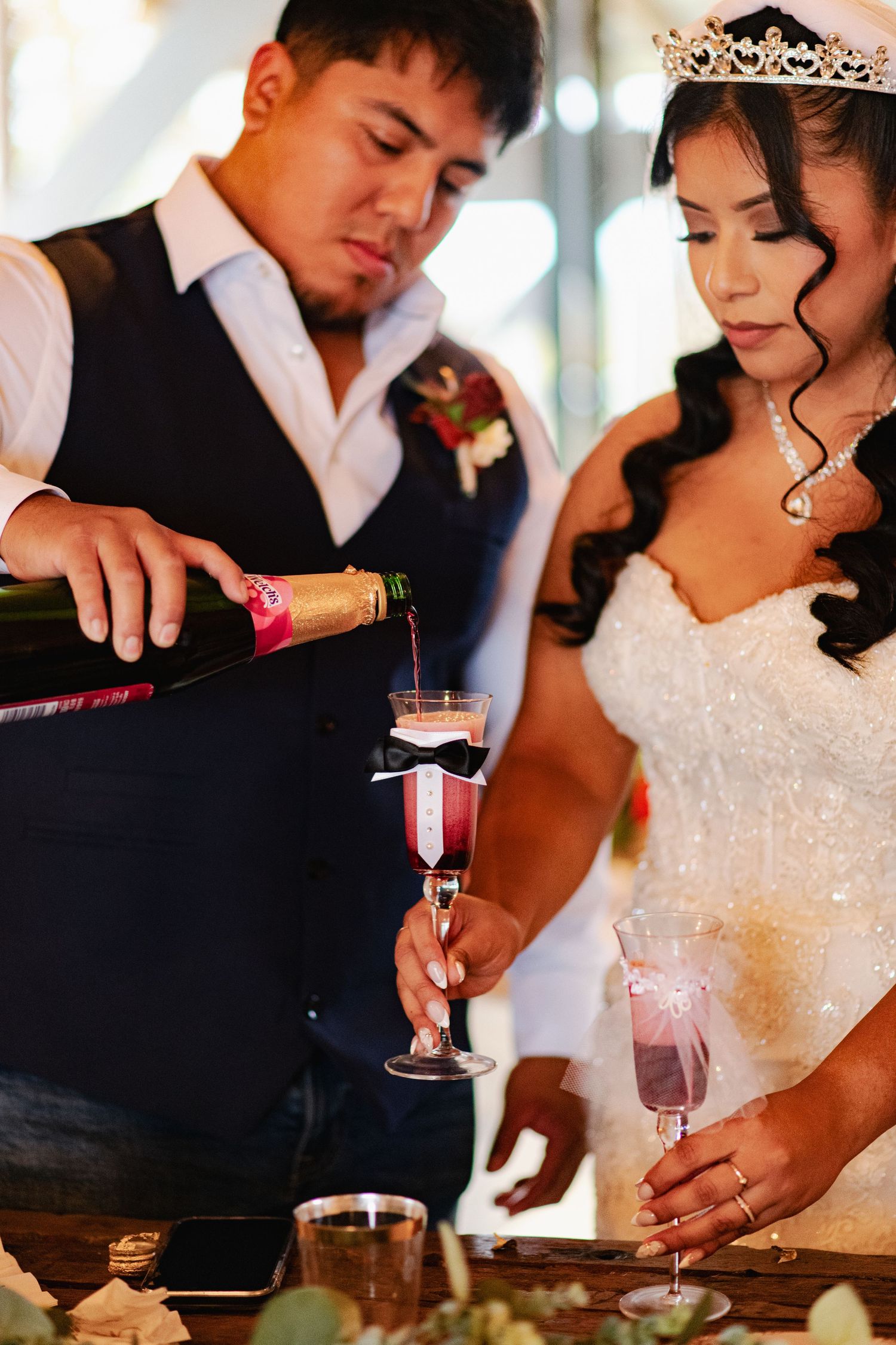 Wedding couple performs champagne pouring ceremony in elegant formal attire.