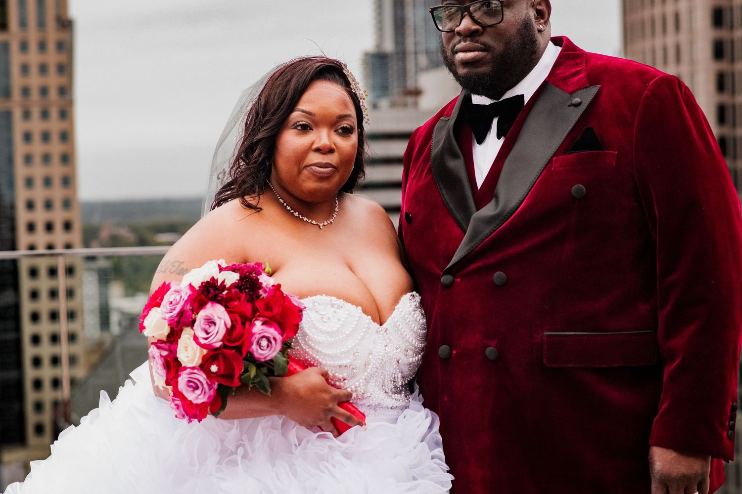 Newlyweds share intimate moments with pink roses against an urban skyline backdrop.