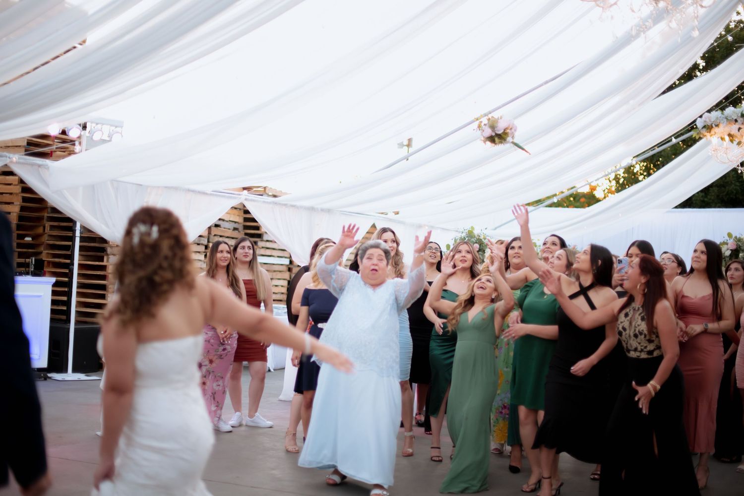 Festive wedding reception scene with guests dancing under white tent decorations.