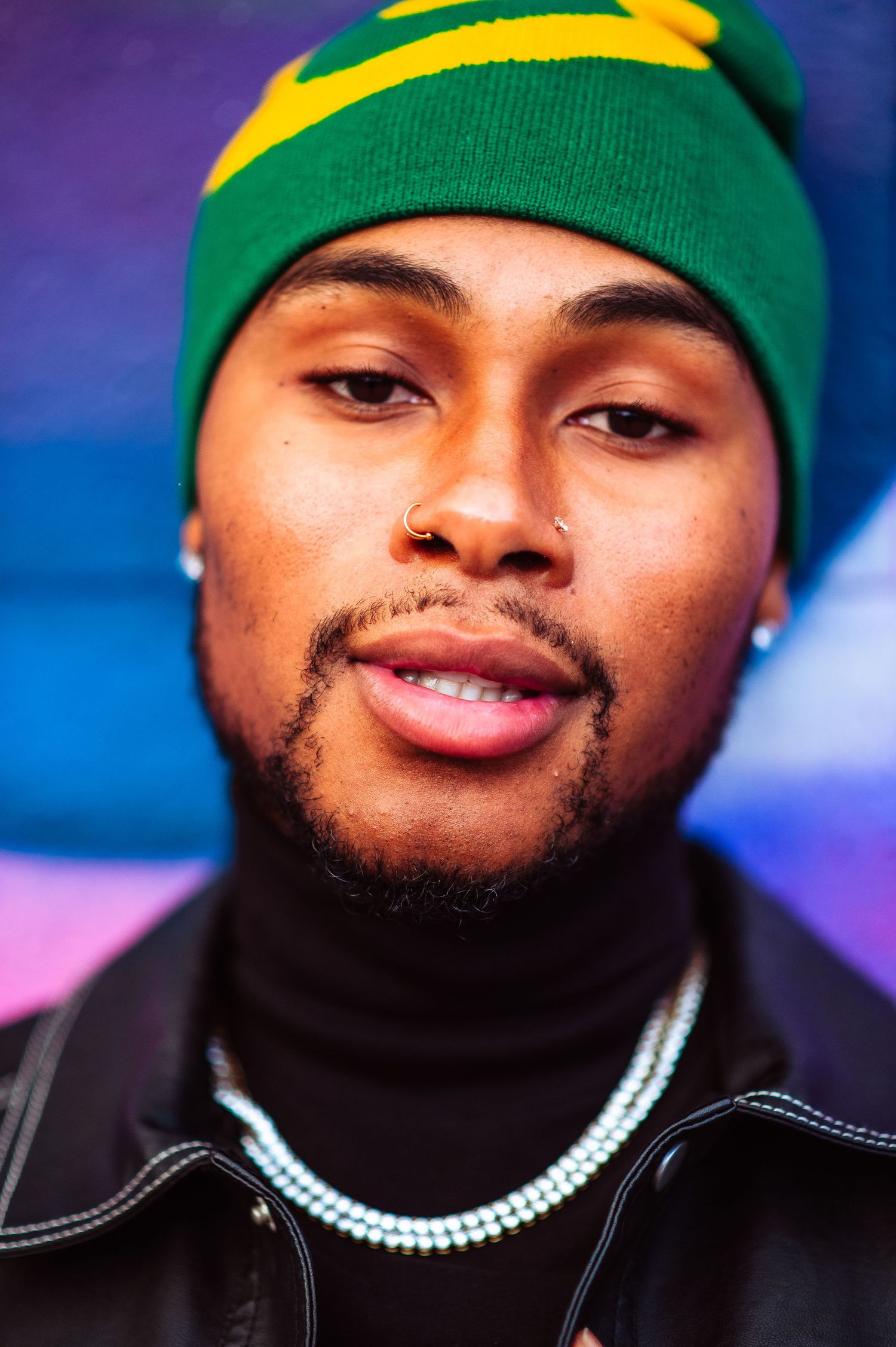 Close up portrait series of someone wearing a green and yellow beanie against a blue background.
