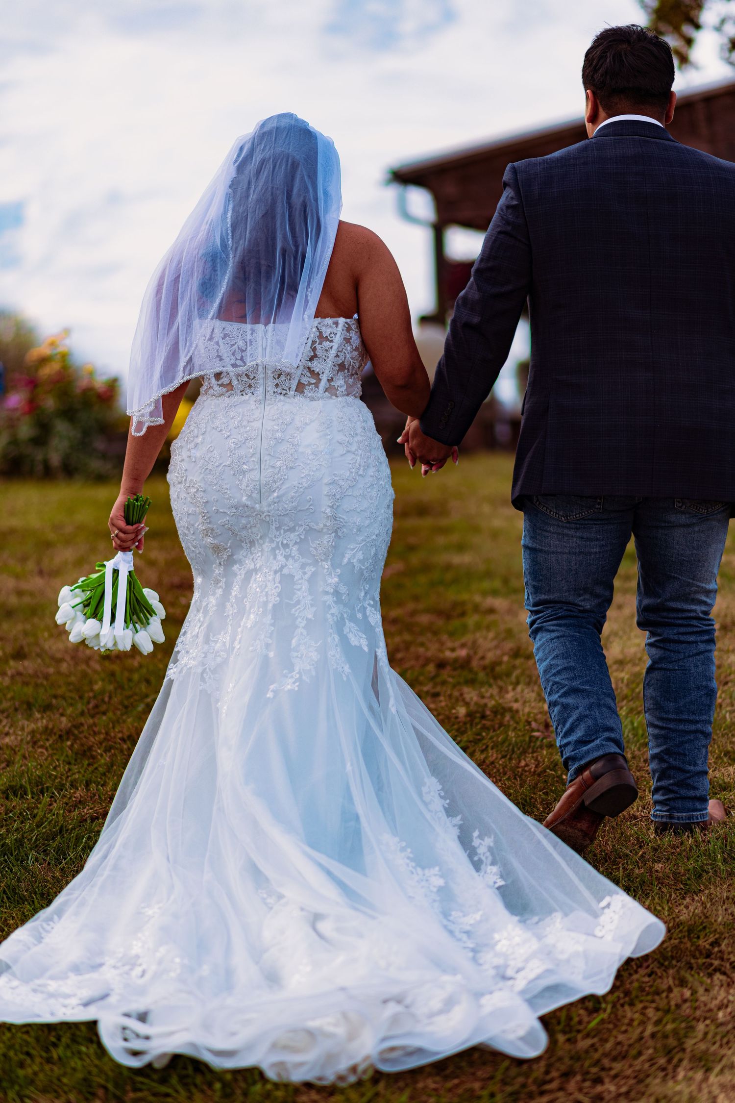 Wedding couple walking in grass with white lace dress and veil trailing behind in a series of romantic shots.