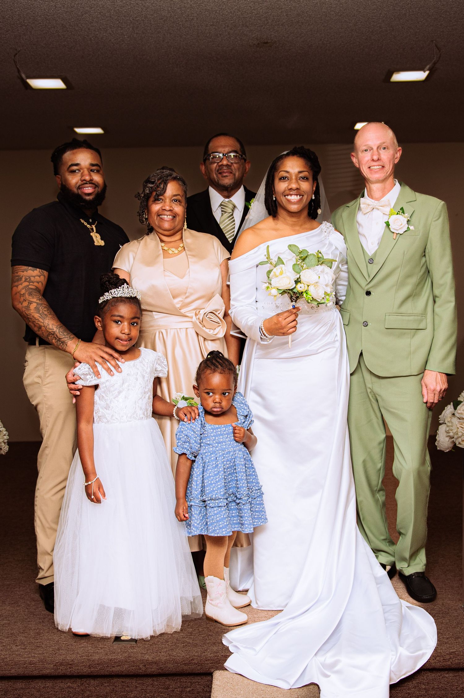 Wedding party members in white dresses and light colored suits gather for formal group photos.