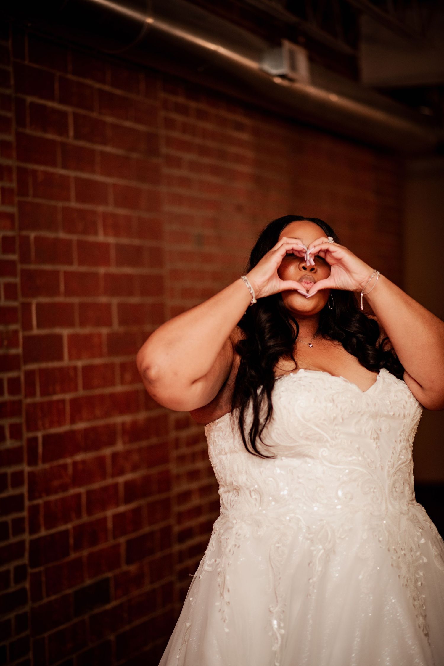 Person in white wedding dress making playful expressions against brick wall.