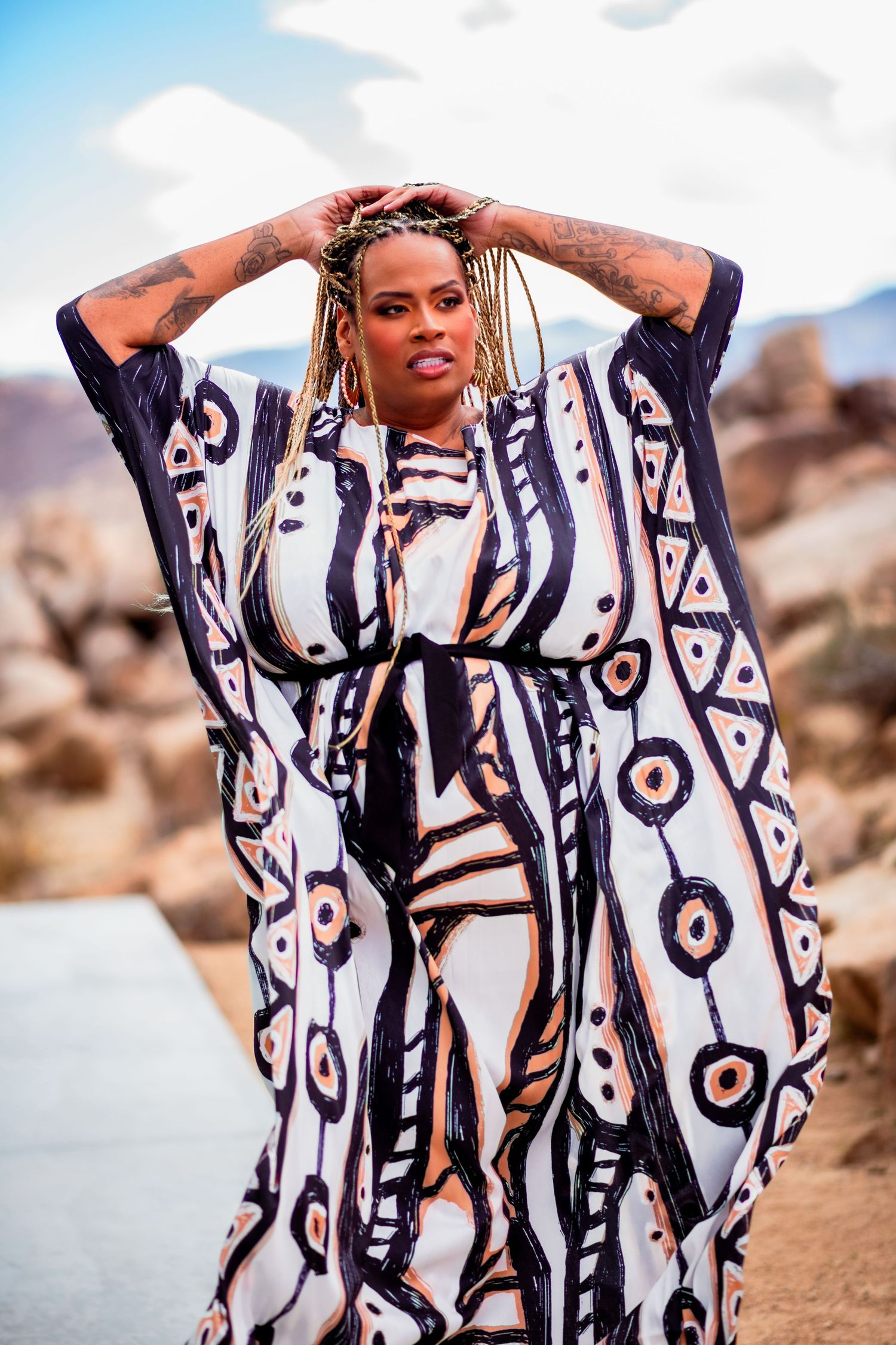 Model wearing black and white patterned kaftan dress poses in desert landscape.