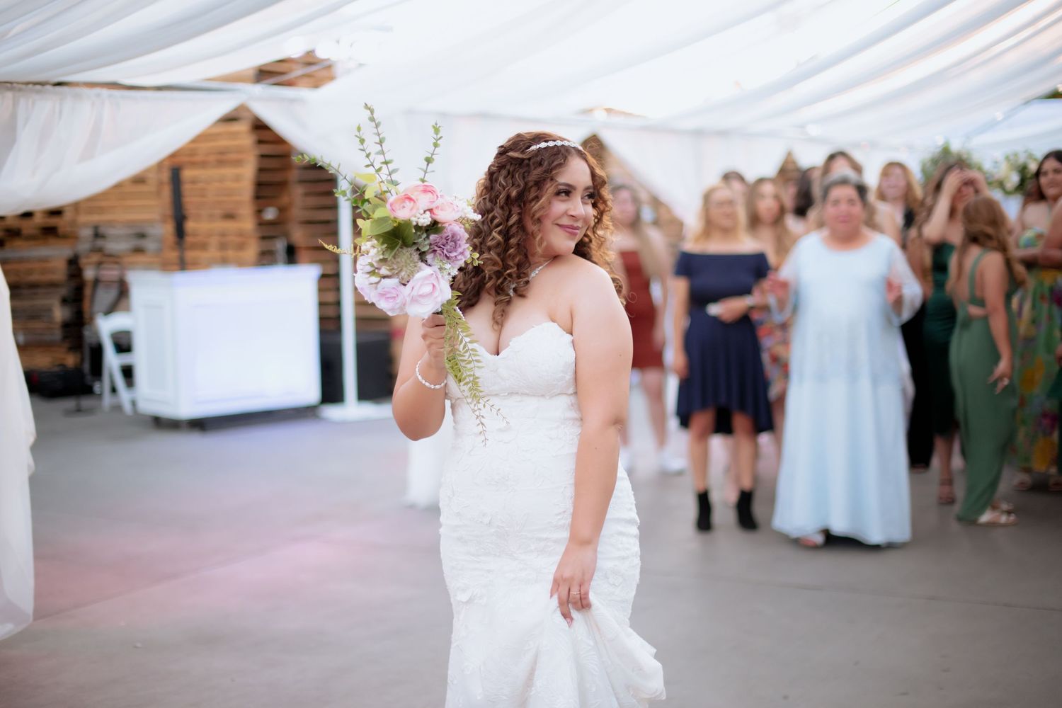 Wedding celebration under a draped white tent with guests mingling and dancing.