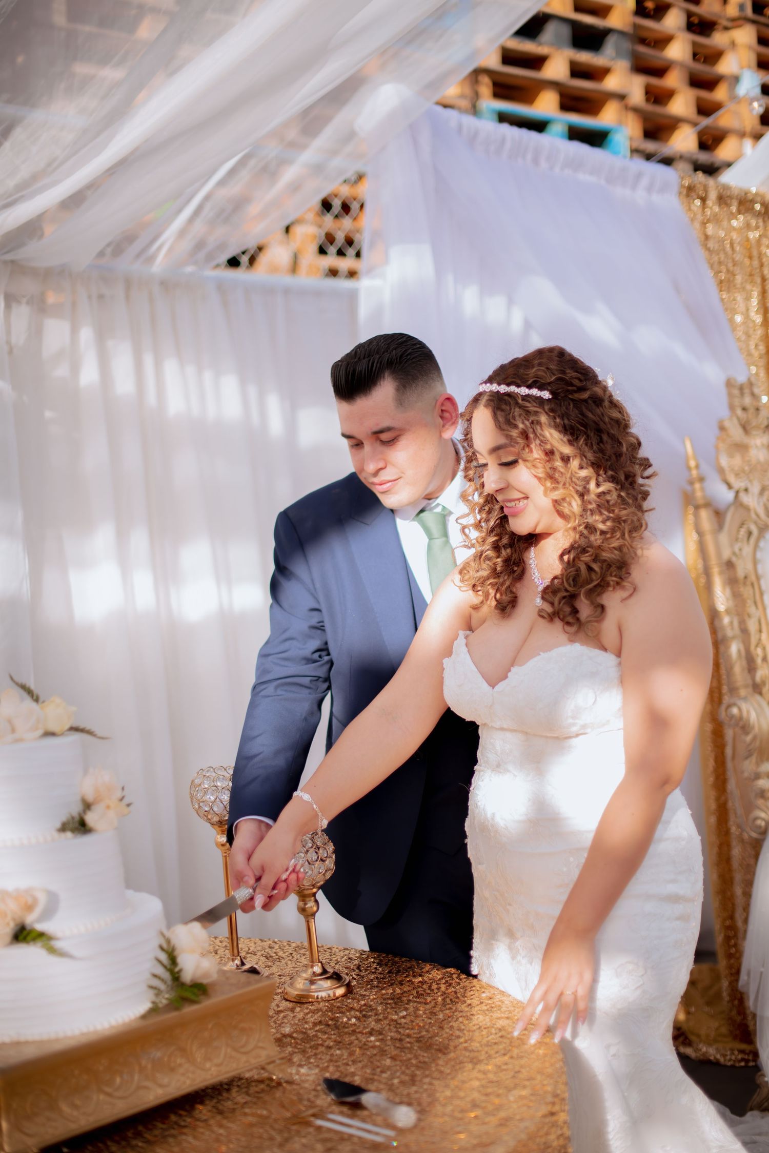 Wedding couple sharing cake at their reception with gold decor and white draping.