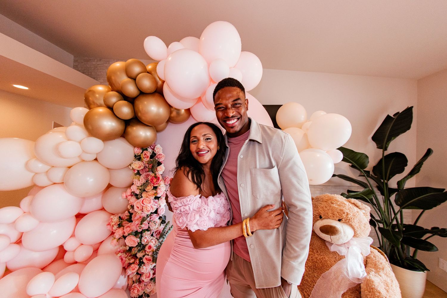 A celebratory setting with pink and gold balloon decorations and floral arrangements.