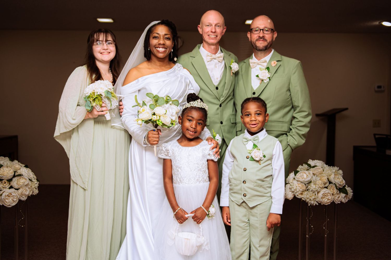 Wedding party poses together wearing sage green and white attire for formal photos.