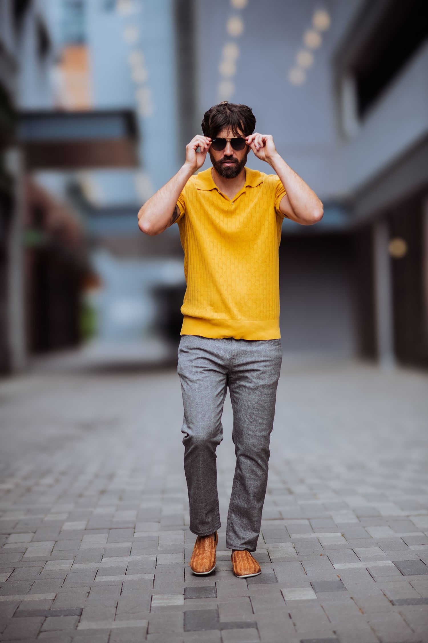 Low angle shot of person in yellow polo and gray pants walking on paved surface.