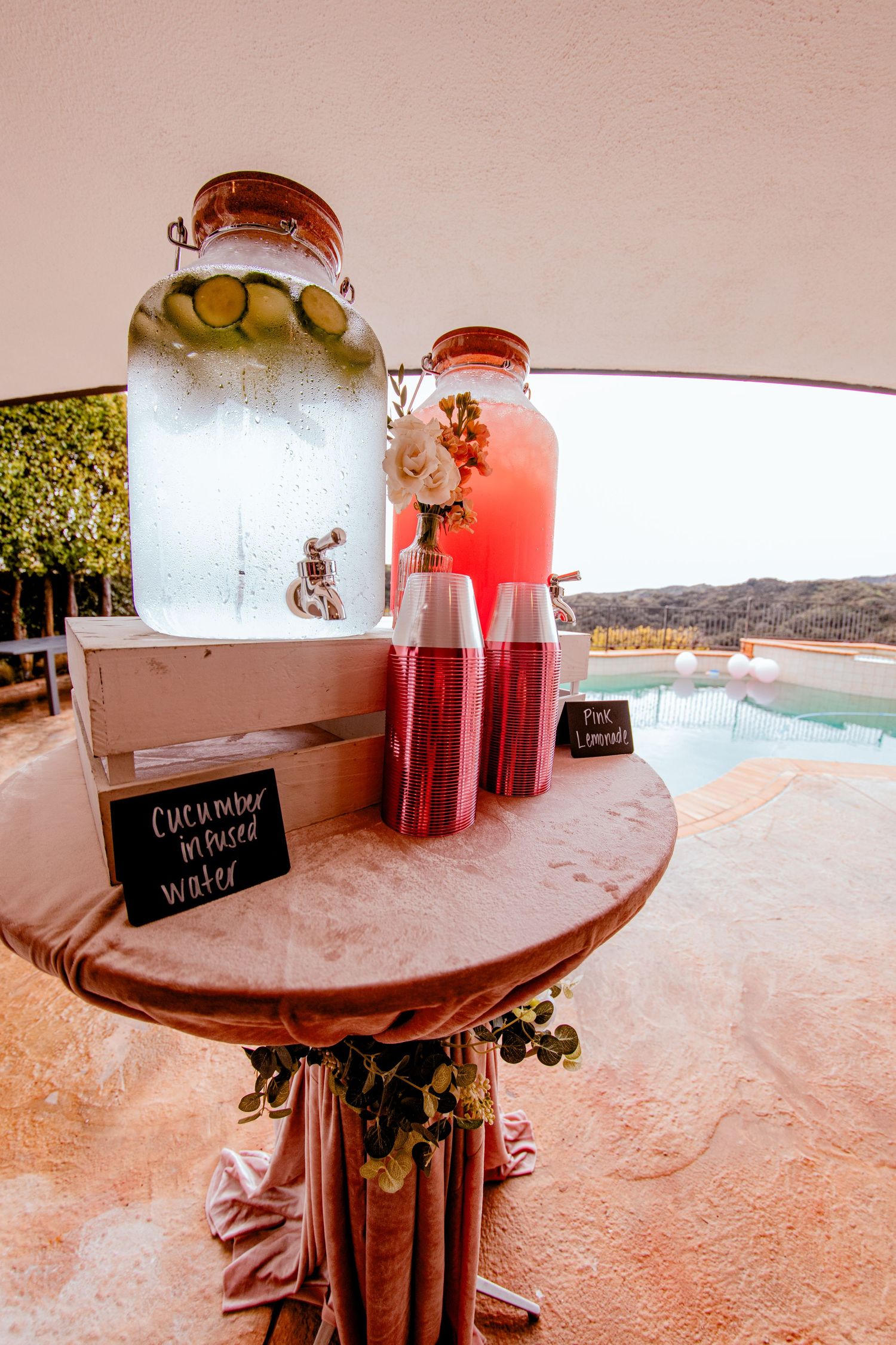 Outdoor beverage station with glass drink dispensers and fresh citrus garnishes by a pool.