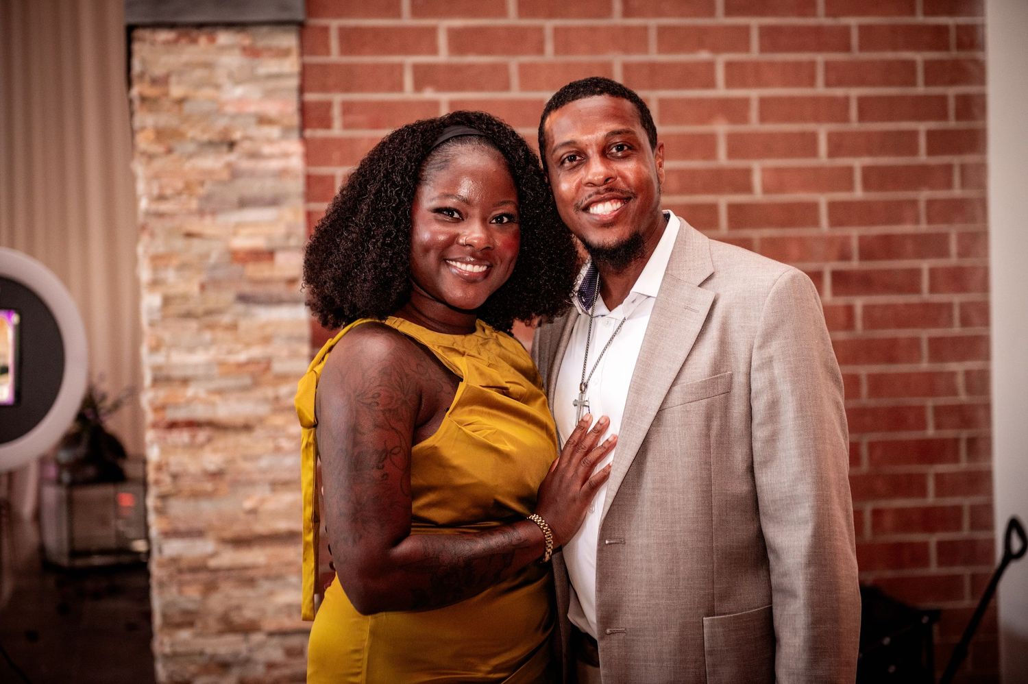 Couple in formal attire posing against rustic brick wall background.