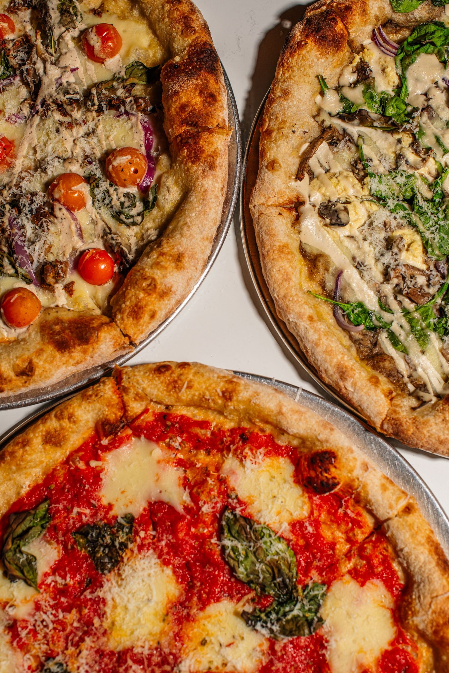Assorted gourmet pizzas with various toppings including tomato sauce, cheese, herbs, and cherry tomatoes on wooden boards.