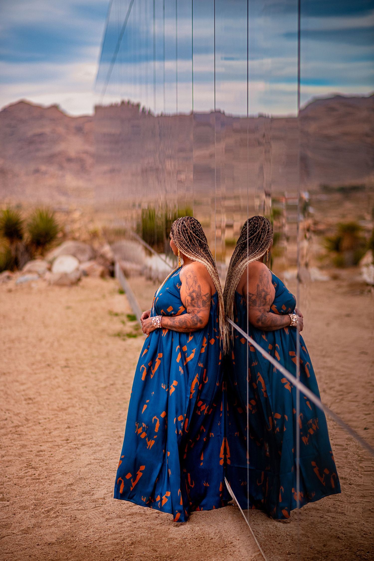 Artistic mirror reflection shoot of person in blue floral dress in desert setting.
