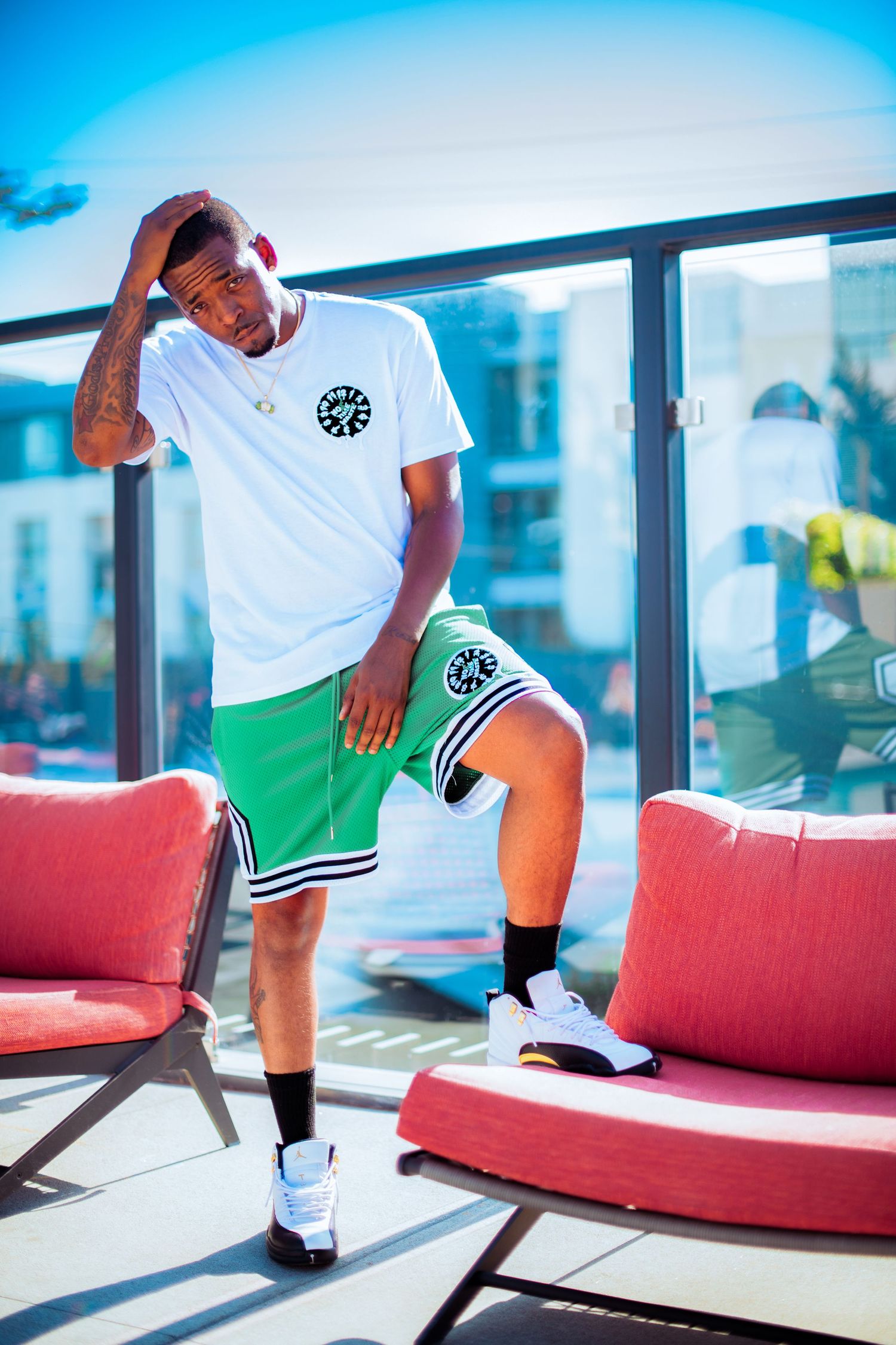 Person in white athletic wear and green shorts lounges on red couch near large windows.