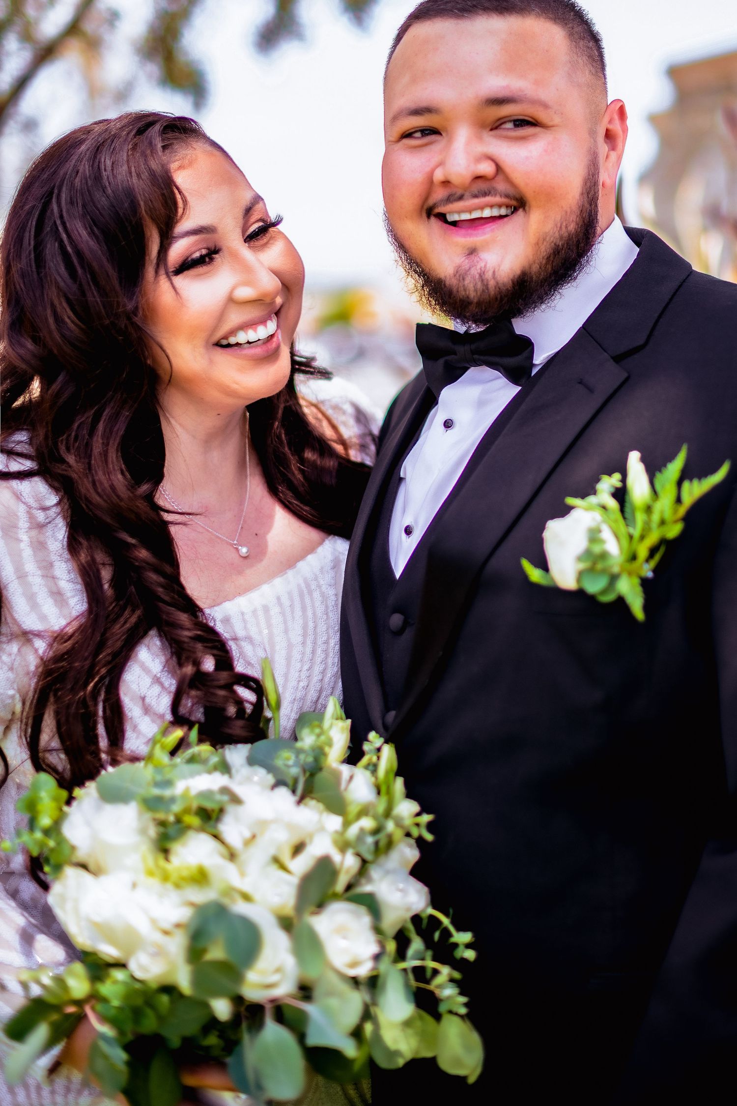 A happy couple shares romantic moments on their wedding day with white floral bouquet and formal attire.