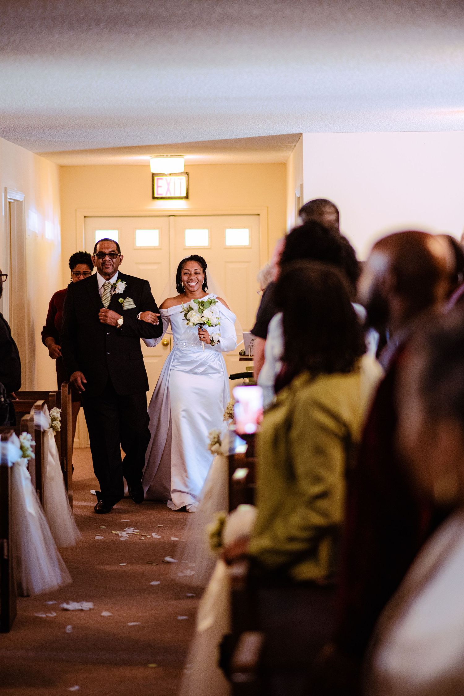 A wedding ceremony processional with a couple walking down the aisle while guests look on in a church interior.