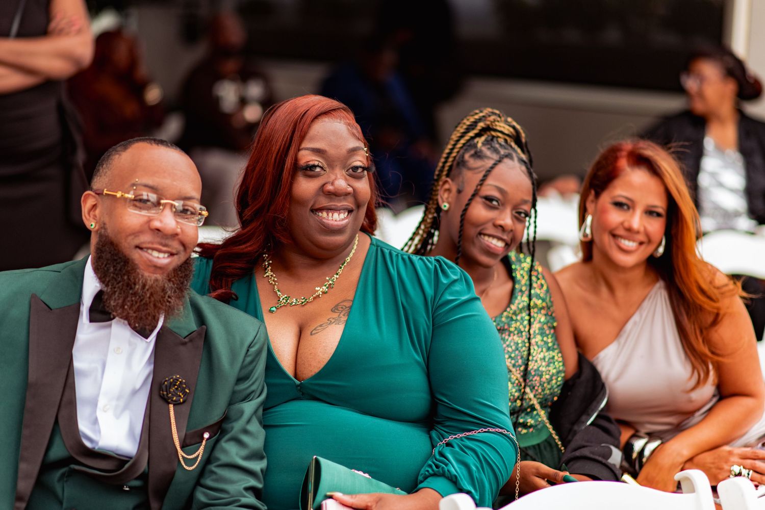 Wedding guests in green and formal attire smile and laugh together during a joyful celebration.