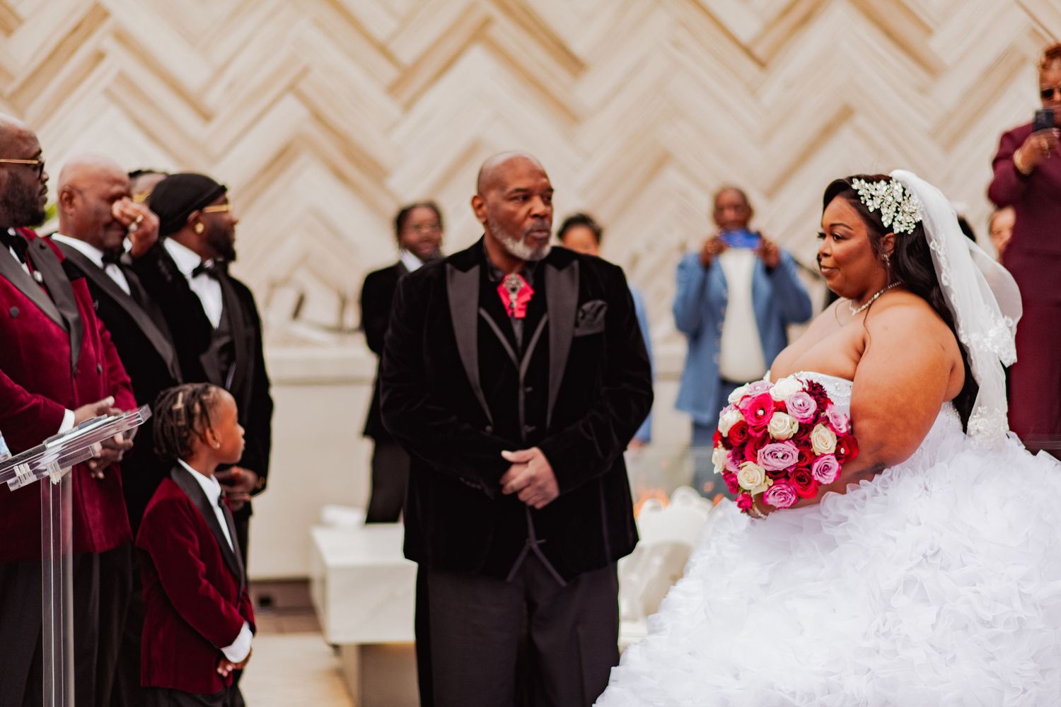 A wedding ceremony in progress with attendants in burgundy attire and white decor.