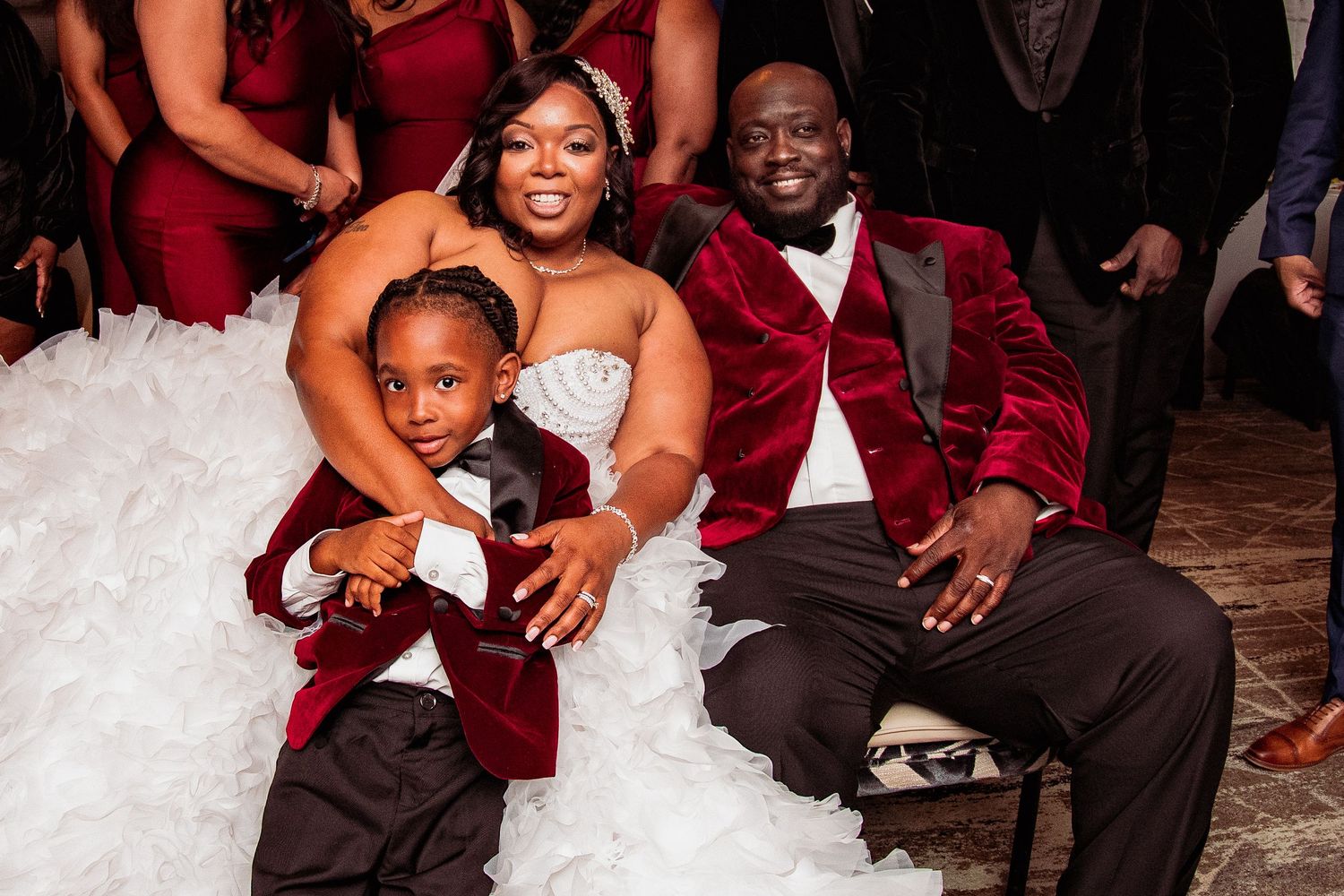 Wedding party members in burgundy and black attire pose together for formal group photos at a celebration.