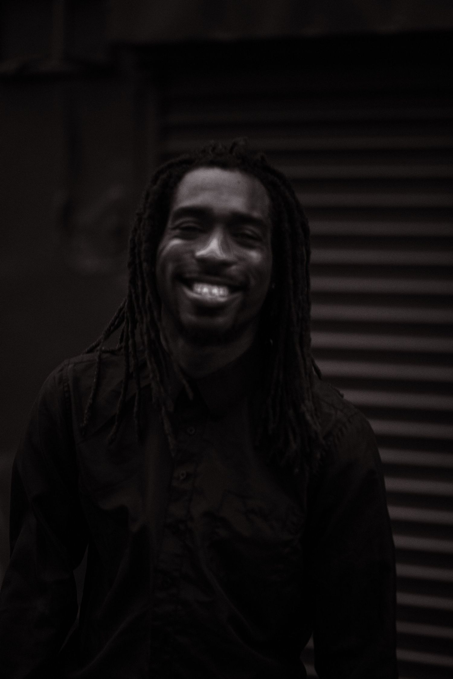 Joyful black and white portrait of person with dreadlocks smiling warmly while wearing dark clothing.