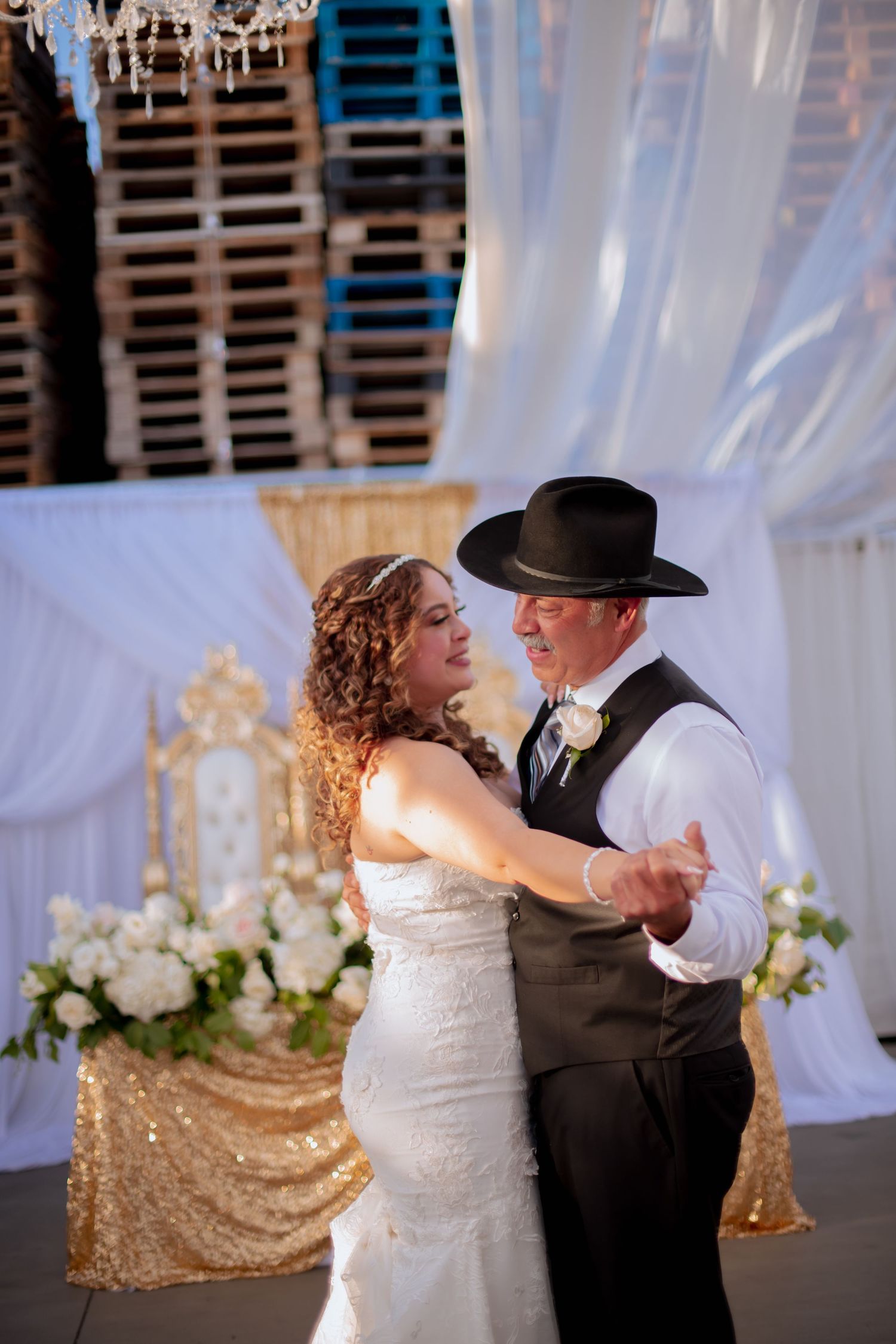 A Father and daughter under sheer white drapes and sparkling chandeliers at wedding.