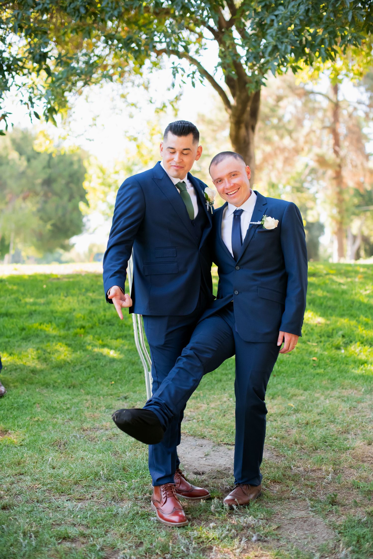 Groomsmen in navy suits show off their shoes in playful outdoor photo.