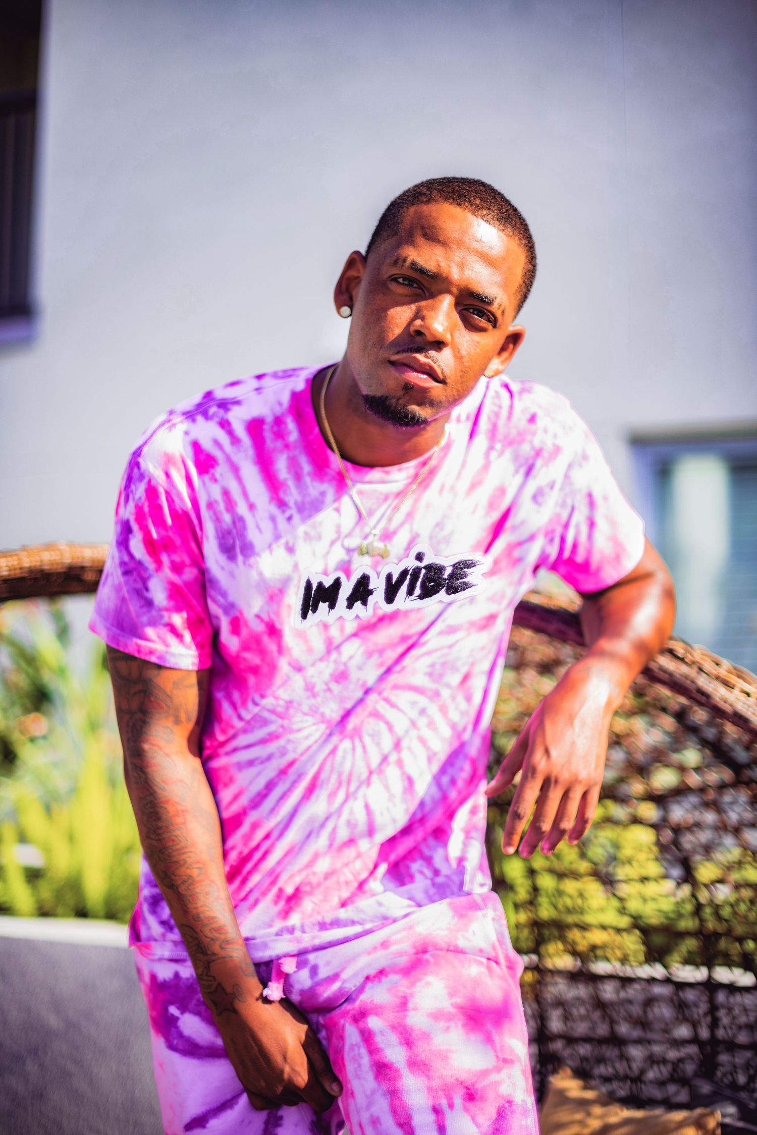 Model wearing pink tie-dye shirt with 'Im a vibe' text poses outdoors in natural lighting.
