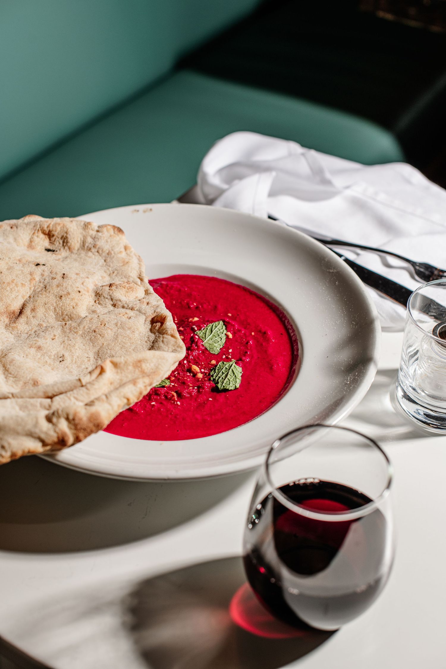 A vibrant red beet dip served on a white plate with homemade flatbread and fresh herbs.