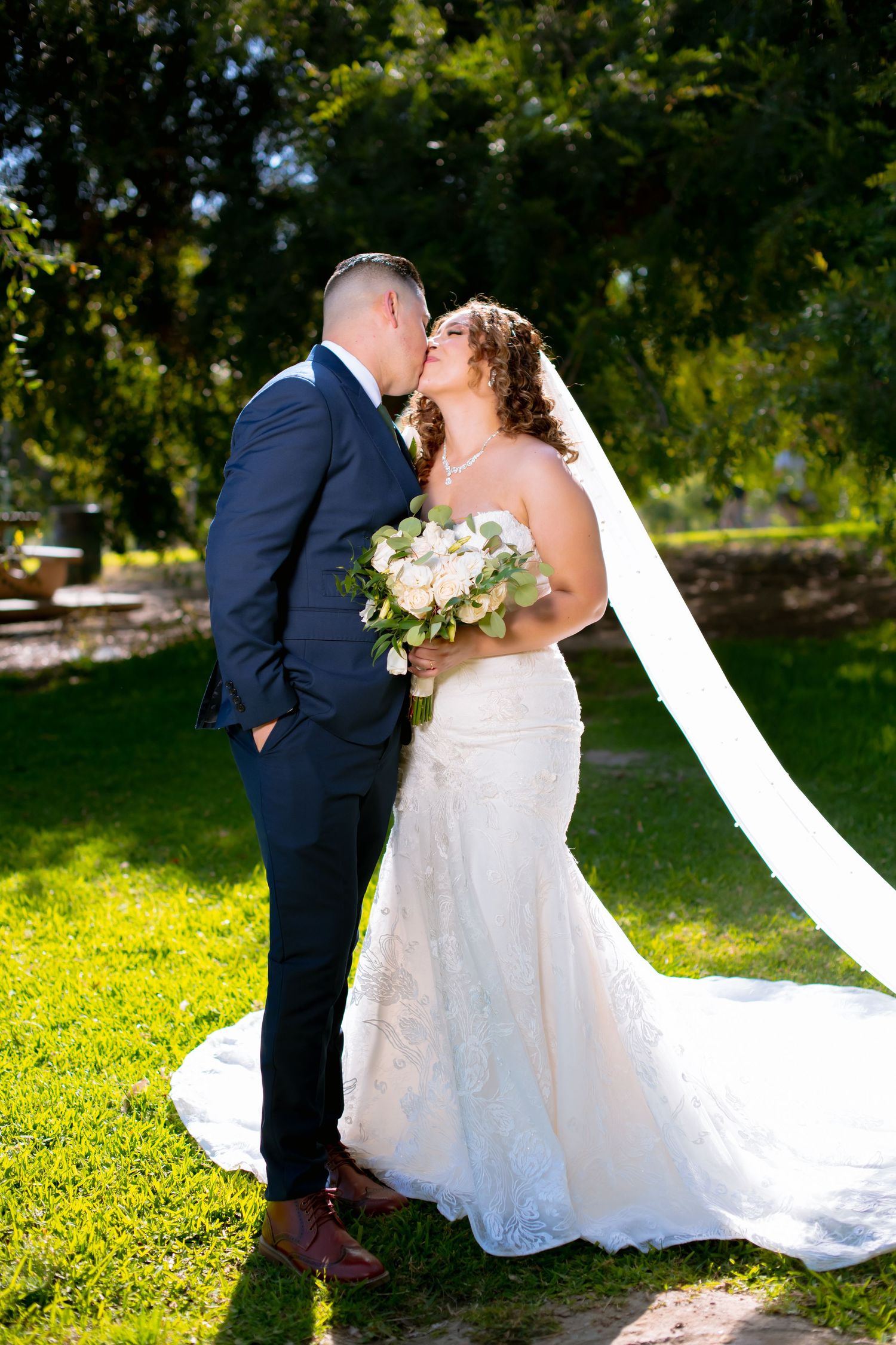 Romantic wedding portraits in a garden setting with flowing white veil and natural sunlight.