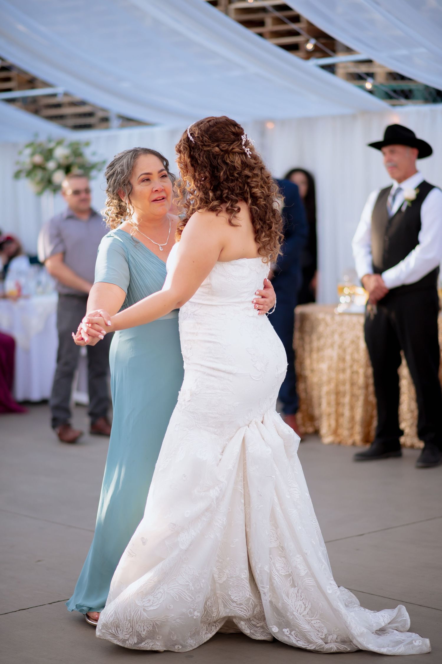 Dancing at wedding reception with white draping and gold sequin backdrop.