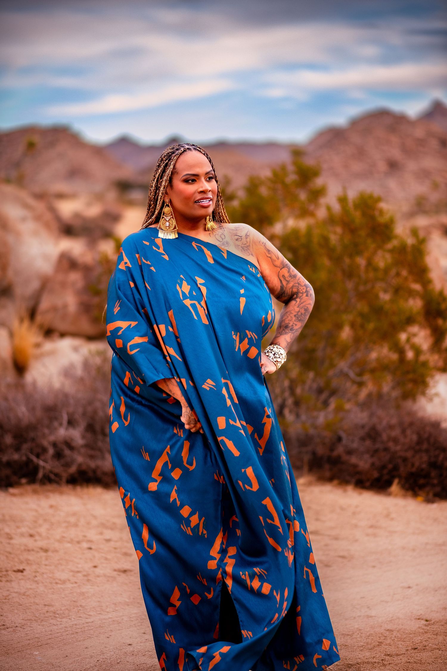Desert photoshoot featuring flowing blue dress with orange accents against mountainous backdrop.