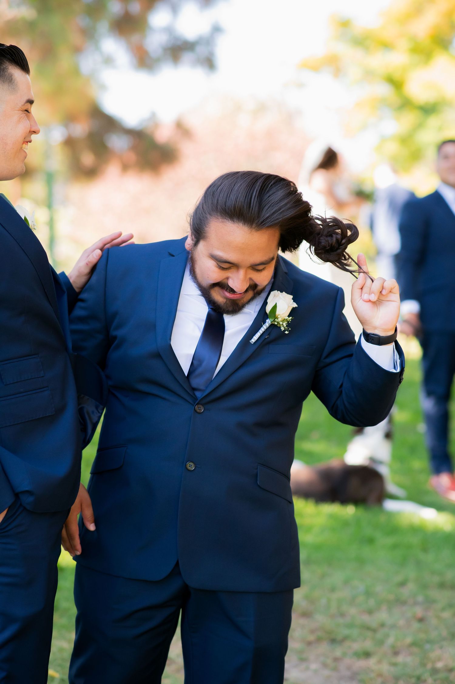 Groomsmen share candid laughing moments in navy suits outdoors.